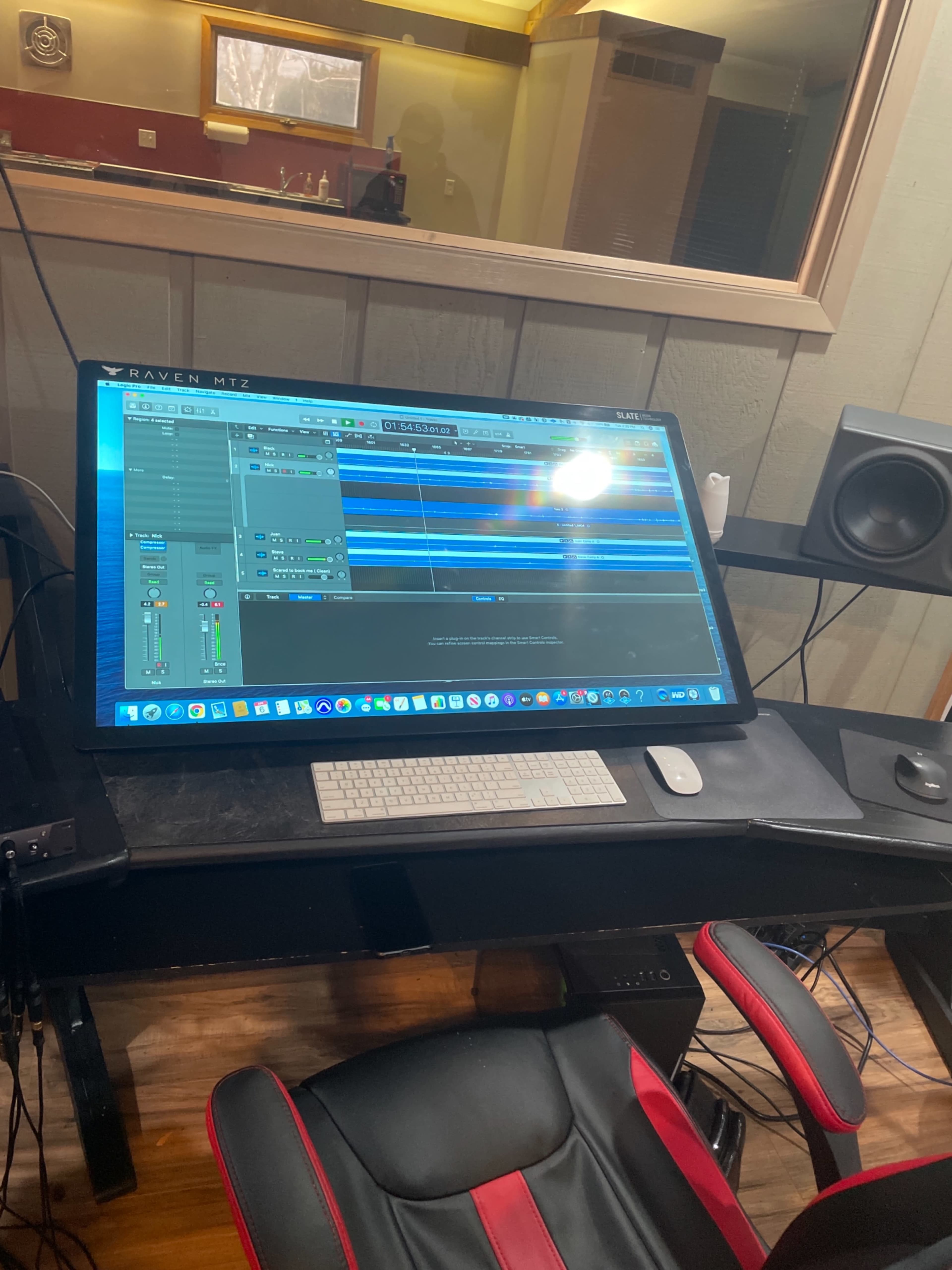 A large computer screen displays a digital audio workstation with multiple tracks and a mixer interface in a recording studio.