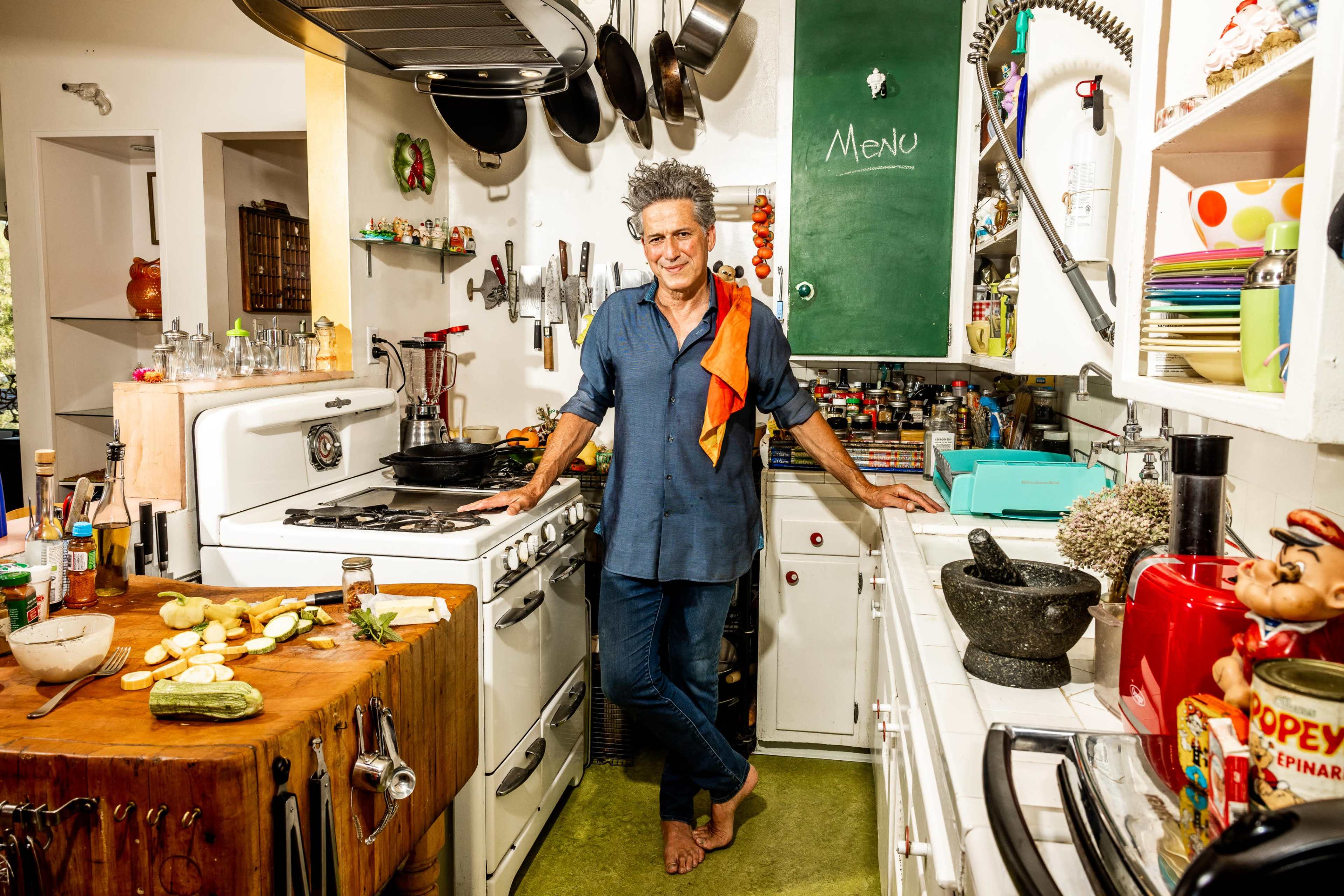 A man stands in a colorful kitchen adorned with various cooking utensils and ingredients spread across the counters.