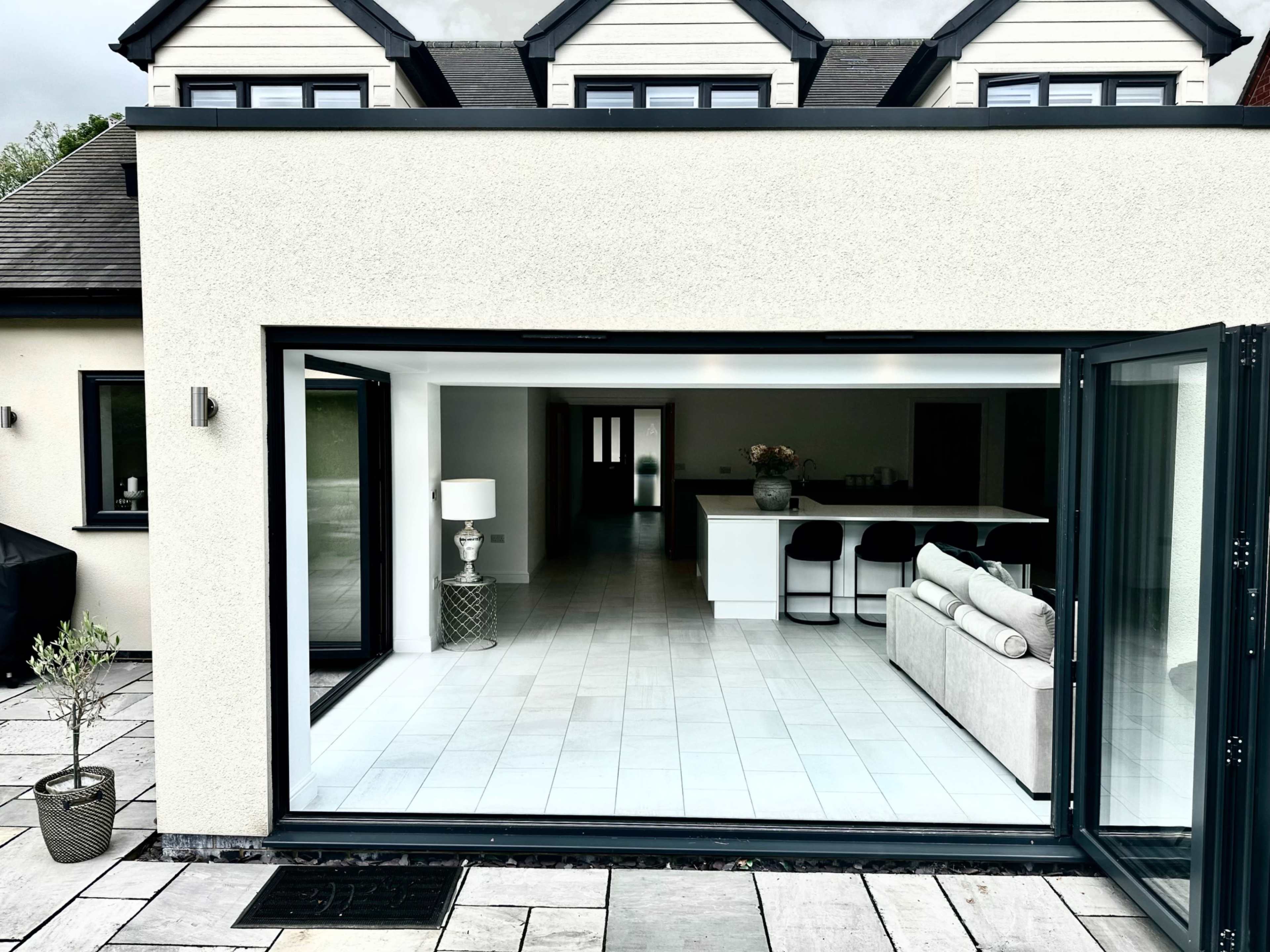 A modern home with large glass doors that open to a spacious interior featuring a kitchen island and a living area.