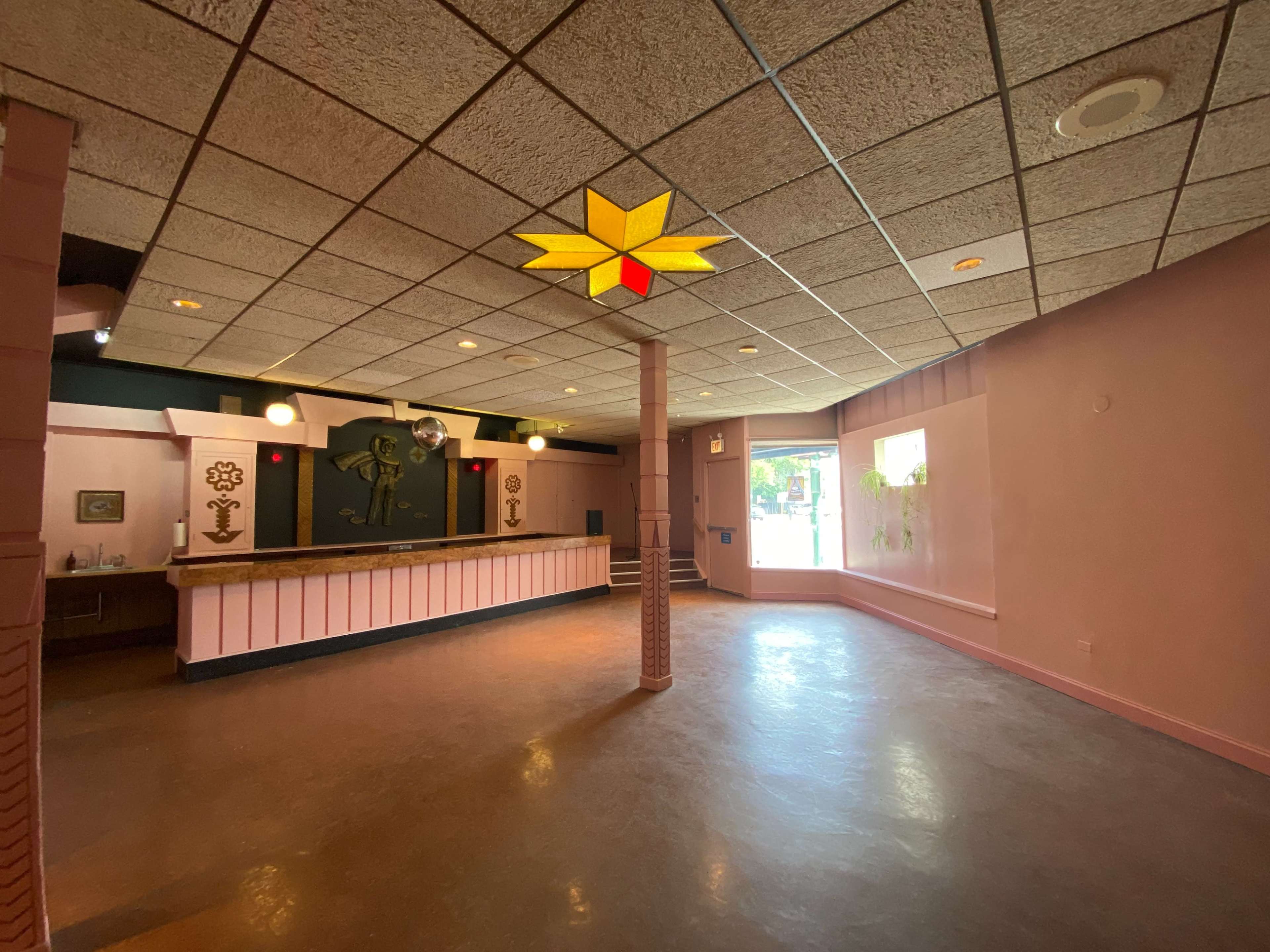 An empty room with a bar area, decorative wall features, and a large window letting in natural light.