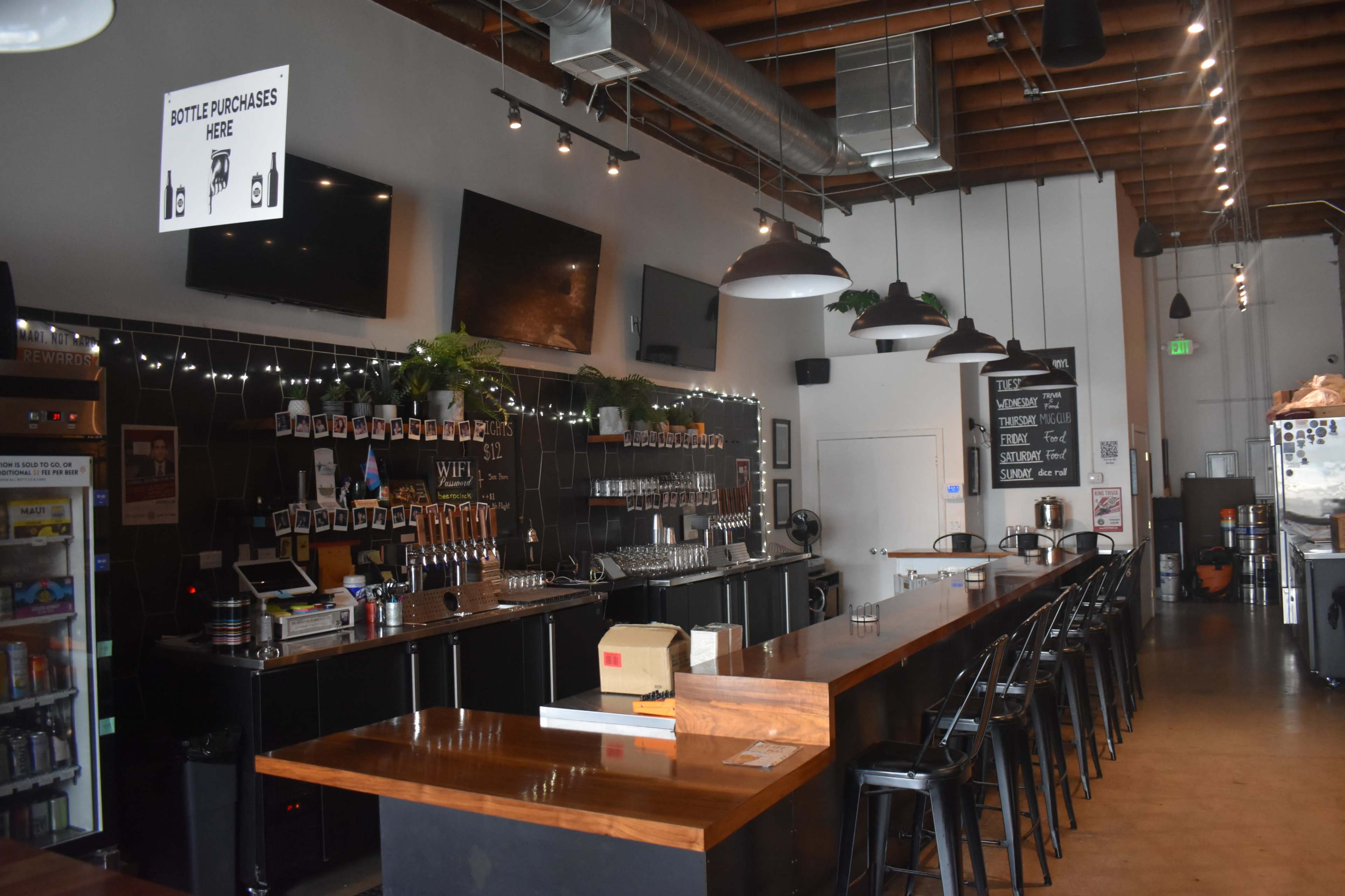 The image shows the interior of a bar with a long wooden counter, multiple seating options, and decorative lighting.