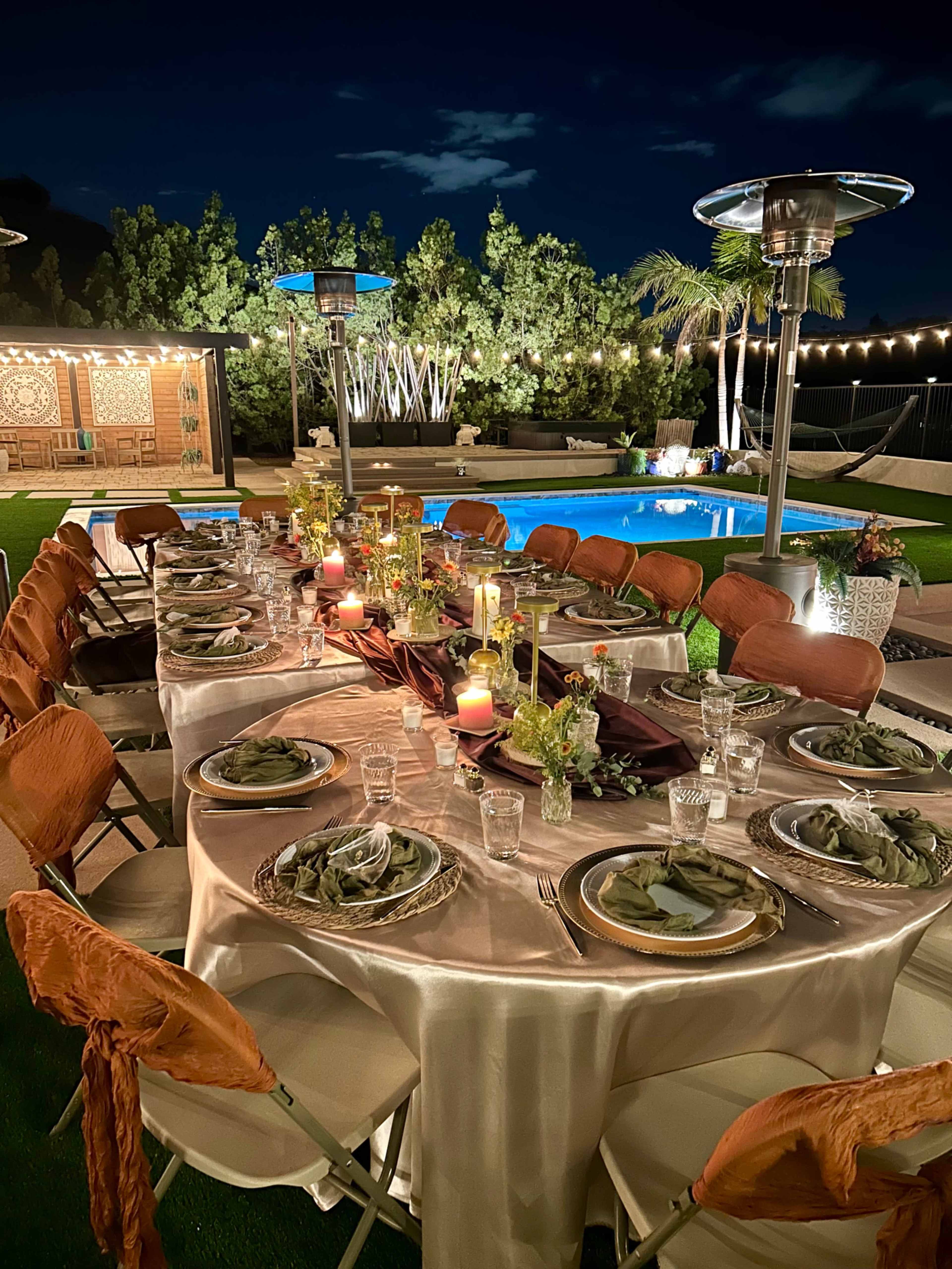 A beautifully set dining table with elegant decor is arranged near a swimming pool in an outdoor setting at night.