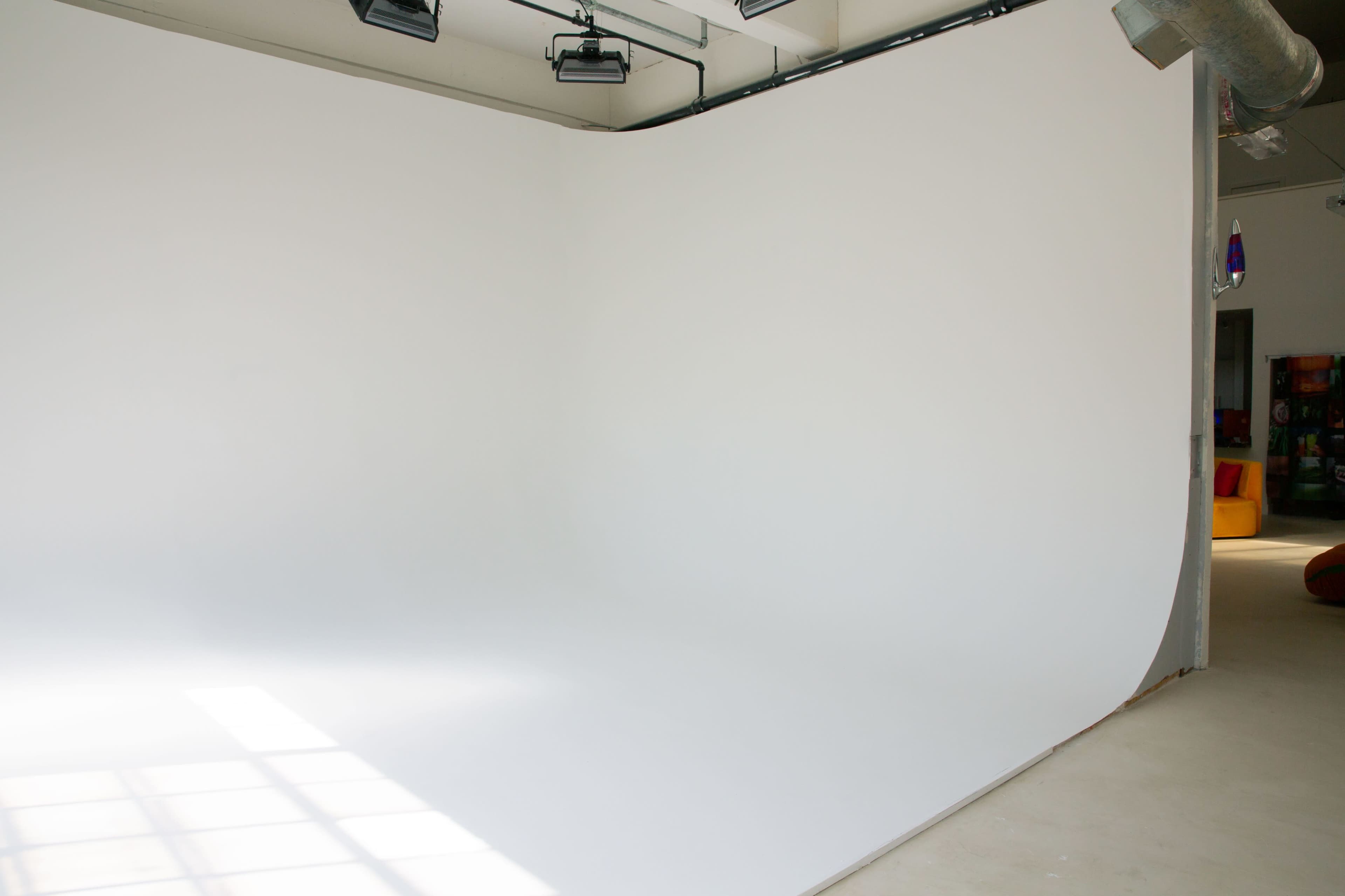 The image shows a spacious studio with a large, curved white backdrop and natural light streaming through windows.