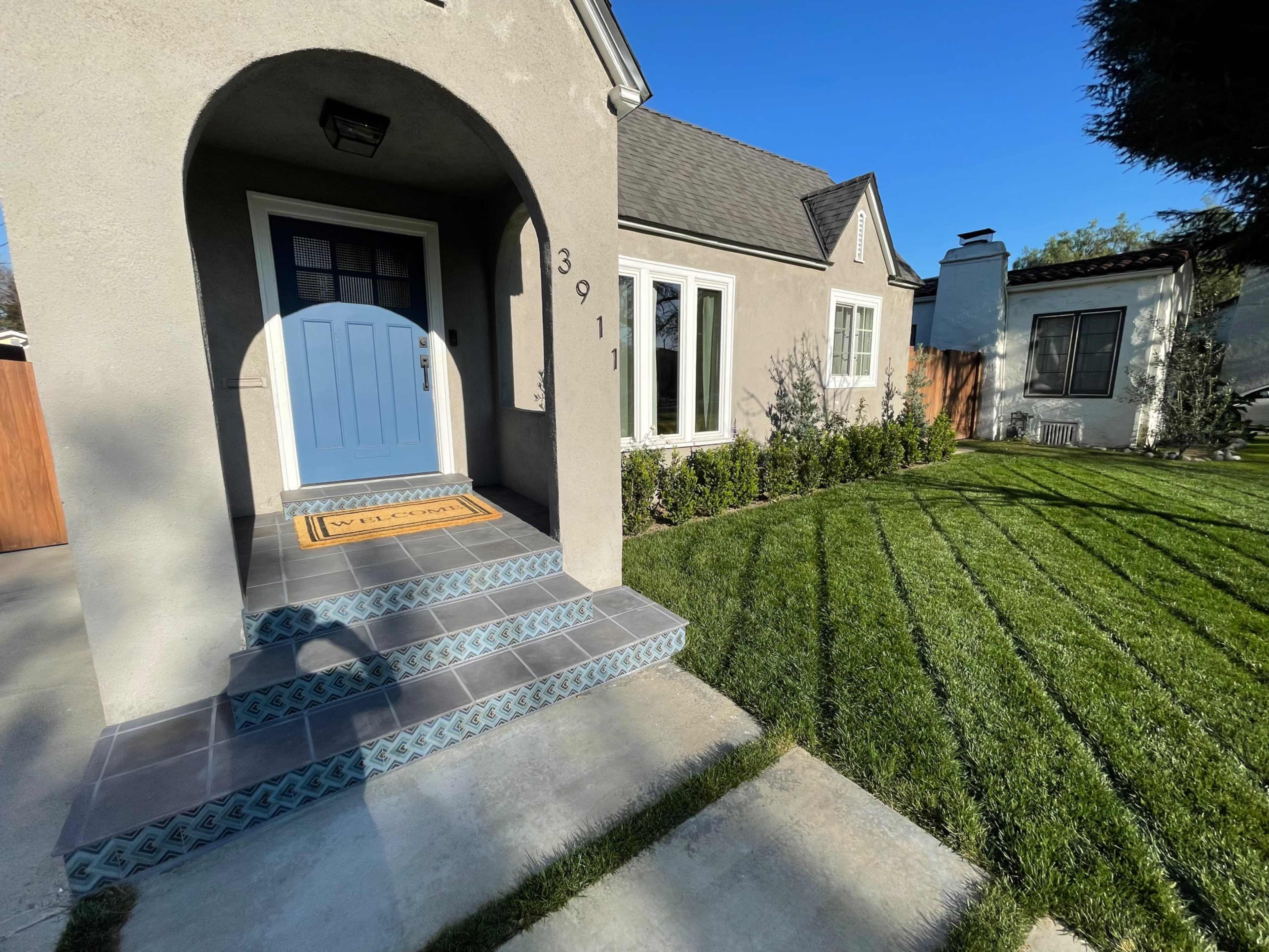 A light blue front door leads to a house with a neat lawn and well-defined landscaping.