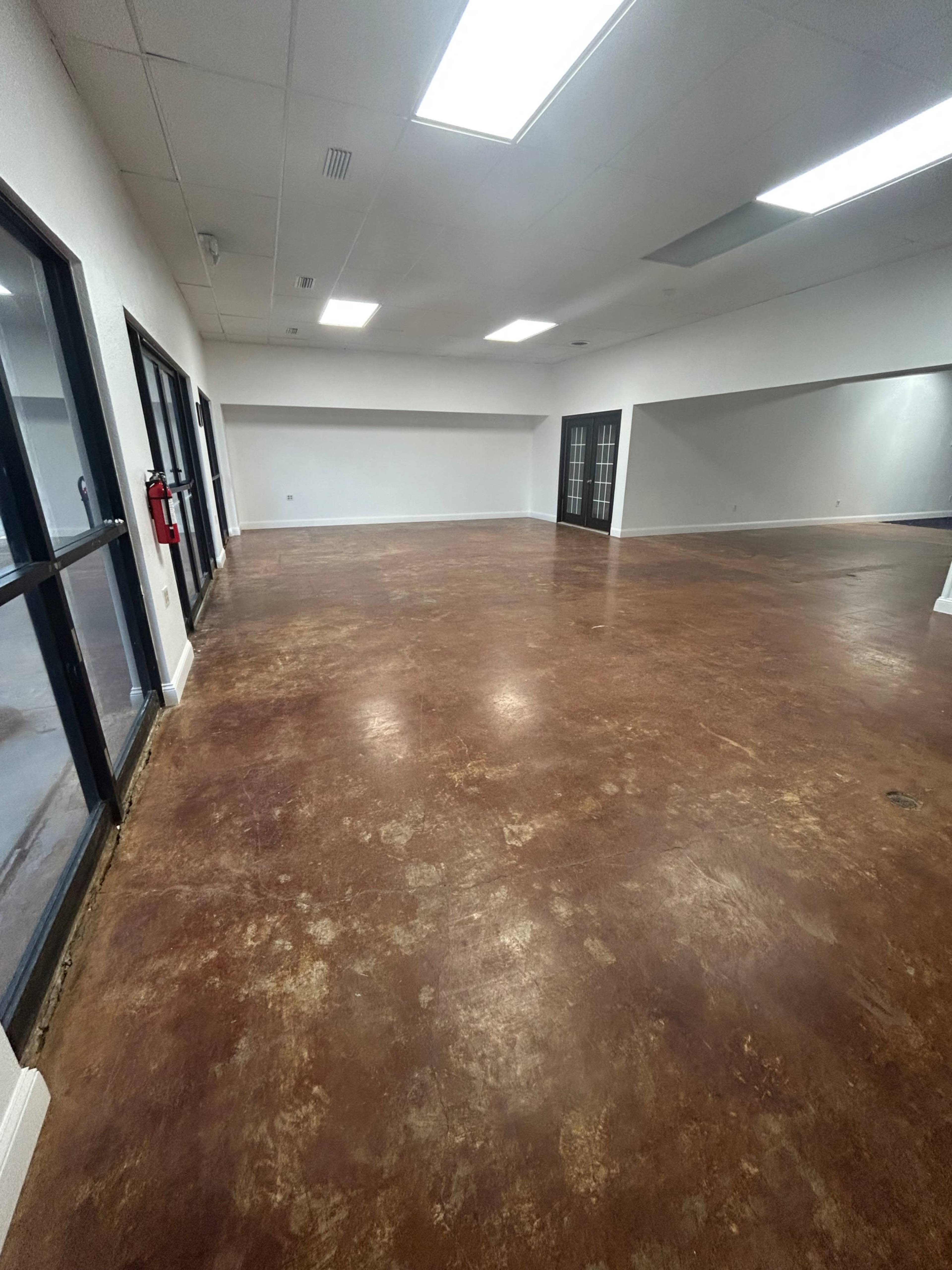 The image shows a large, empty room with a polished concrete floor and multiple windows.