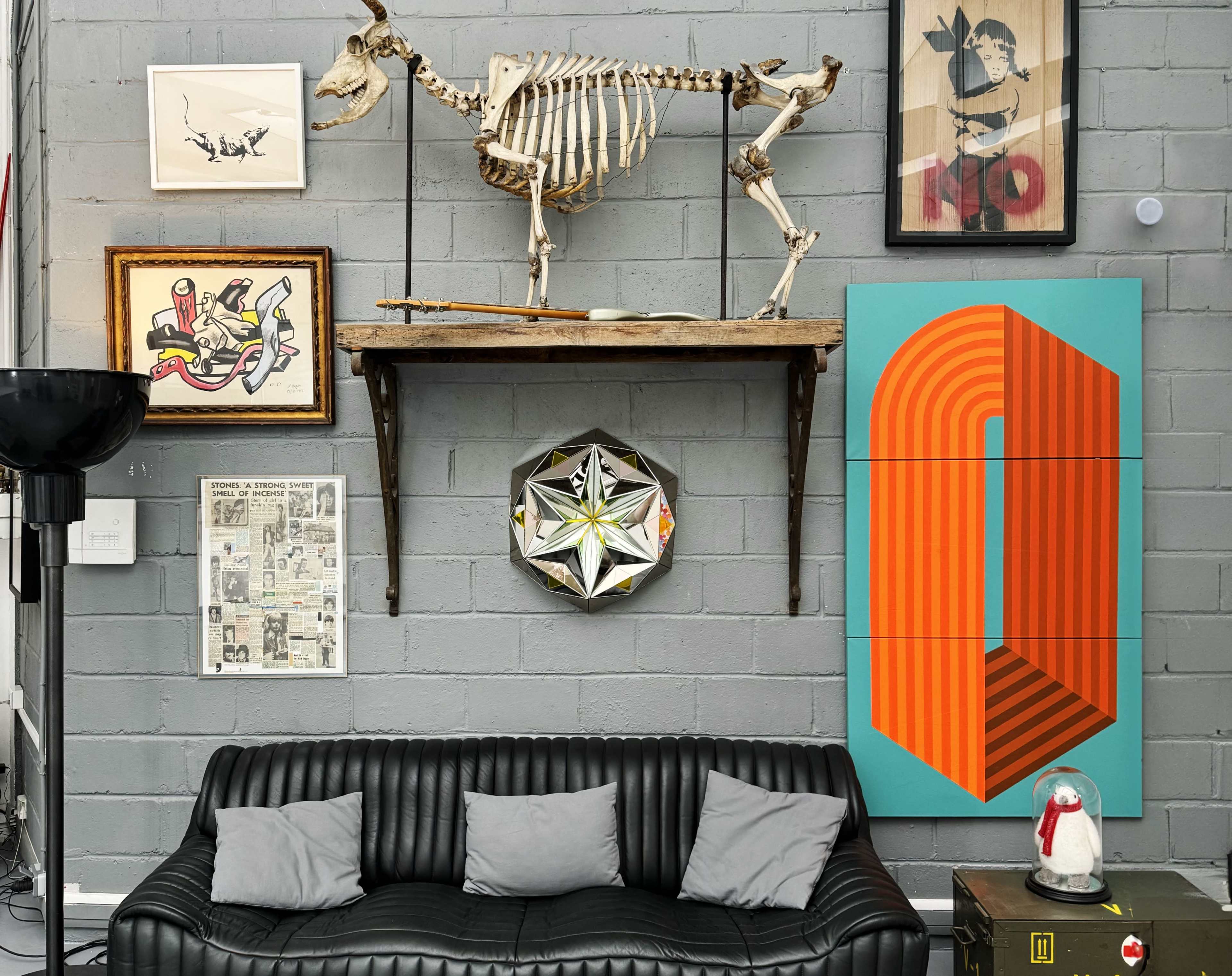 A modern interior wall featuring a skeleton display, framed artwork, and a black leather couch with gray cushions.