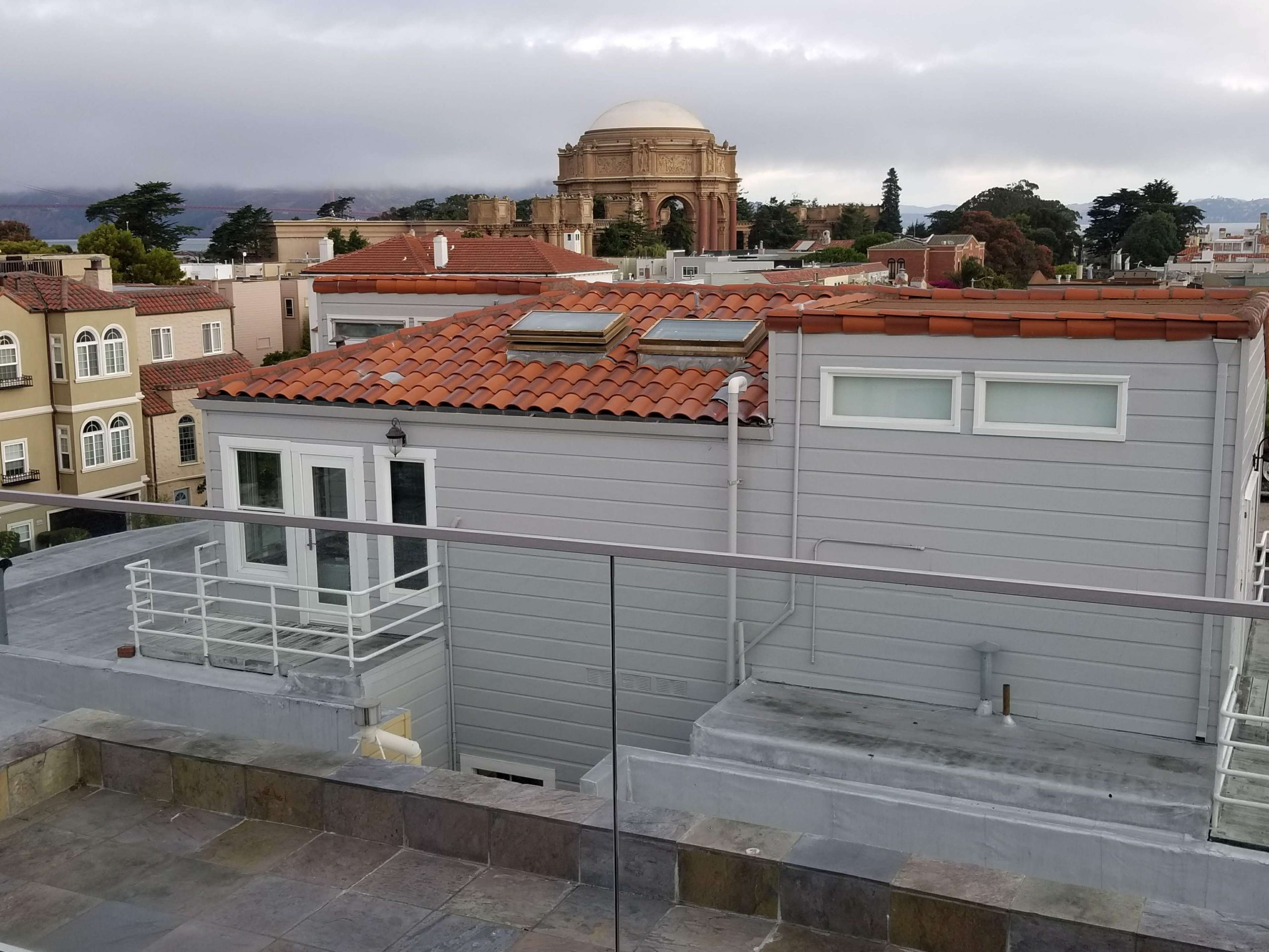 A rooftop view of buildings with red-tiled roofs, overlooking a dome structure in the distance.
