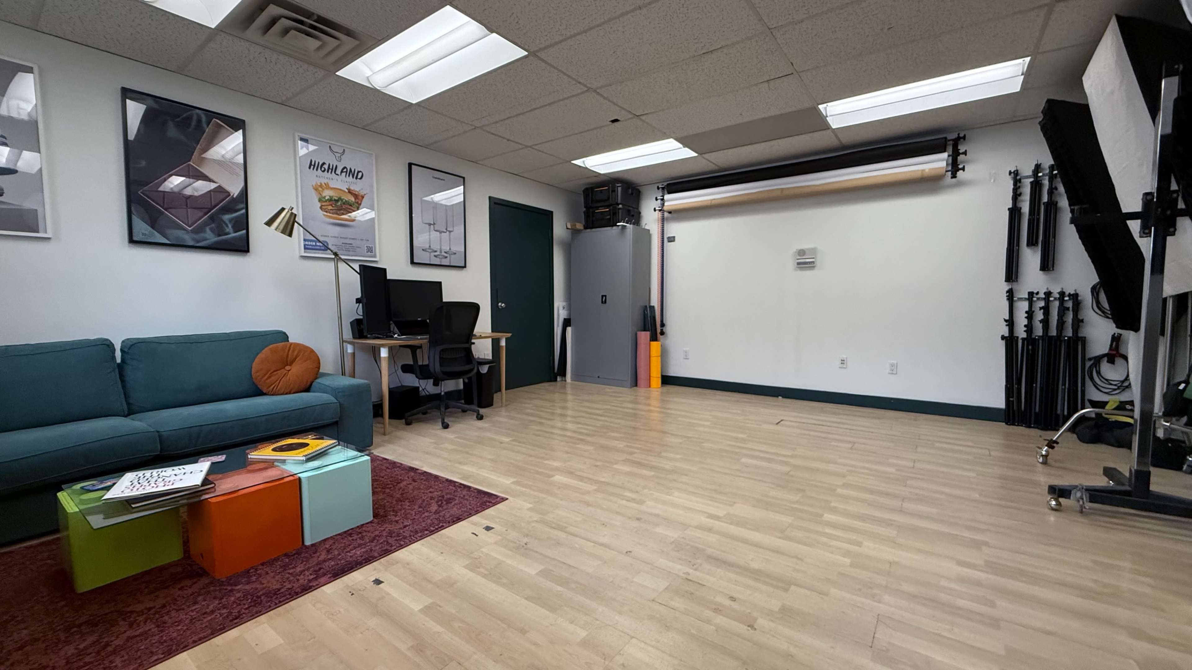 The image shows a spacious studio room with a green couch, a desk with a computer, and various photography equipment along the walls.