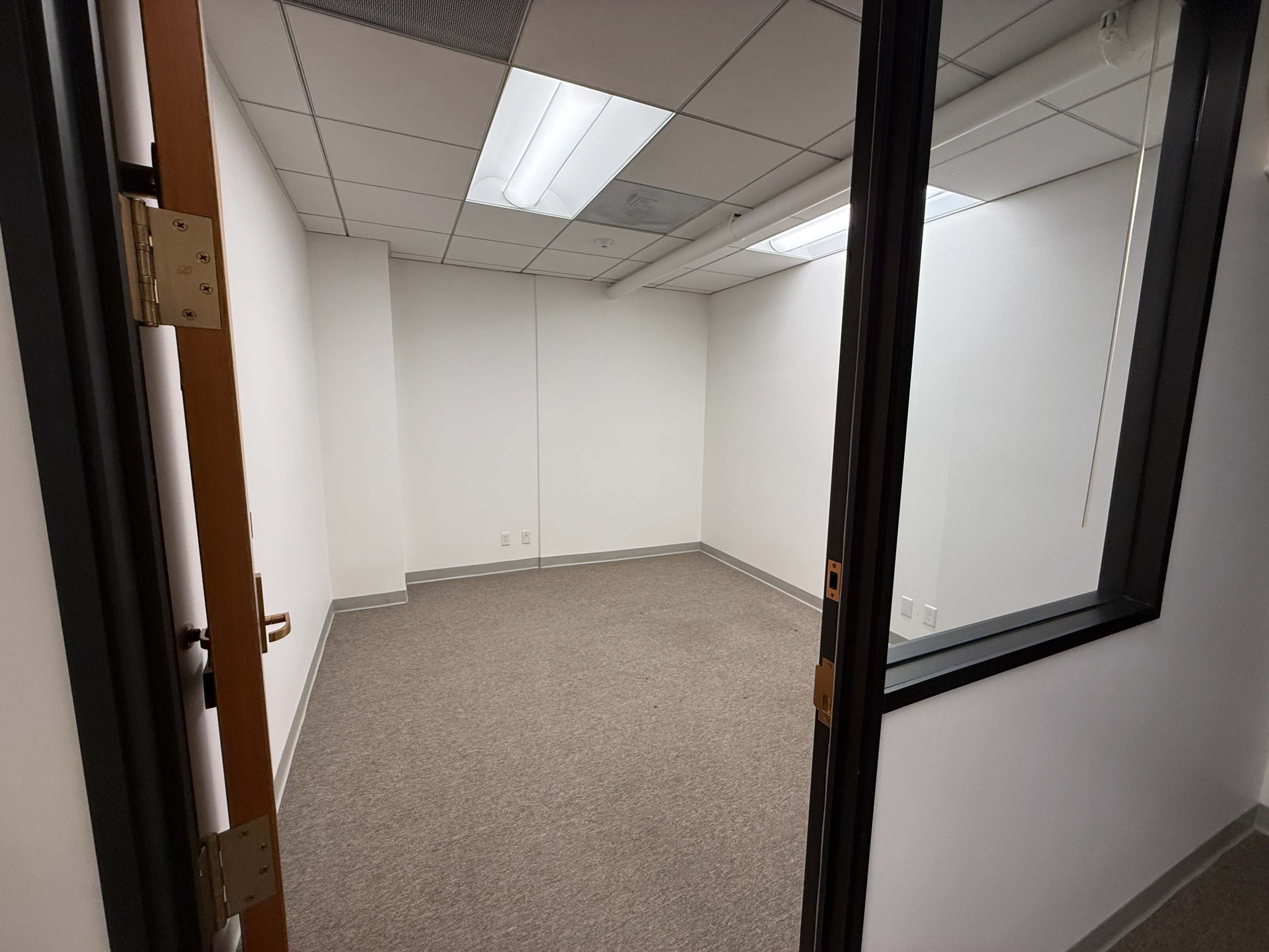 The image shows an empty office space with beige carpet and white walls.