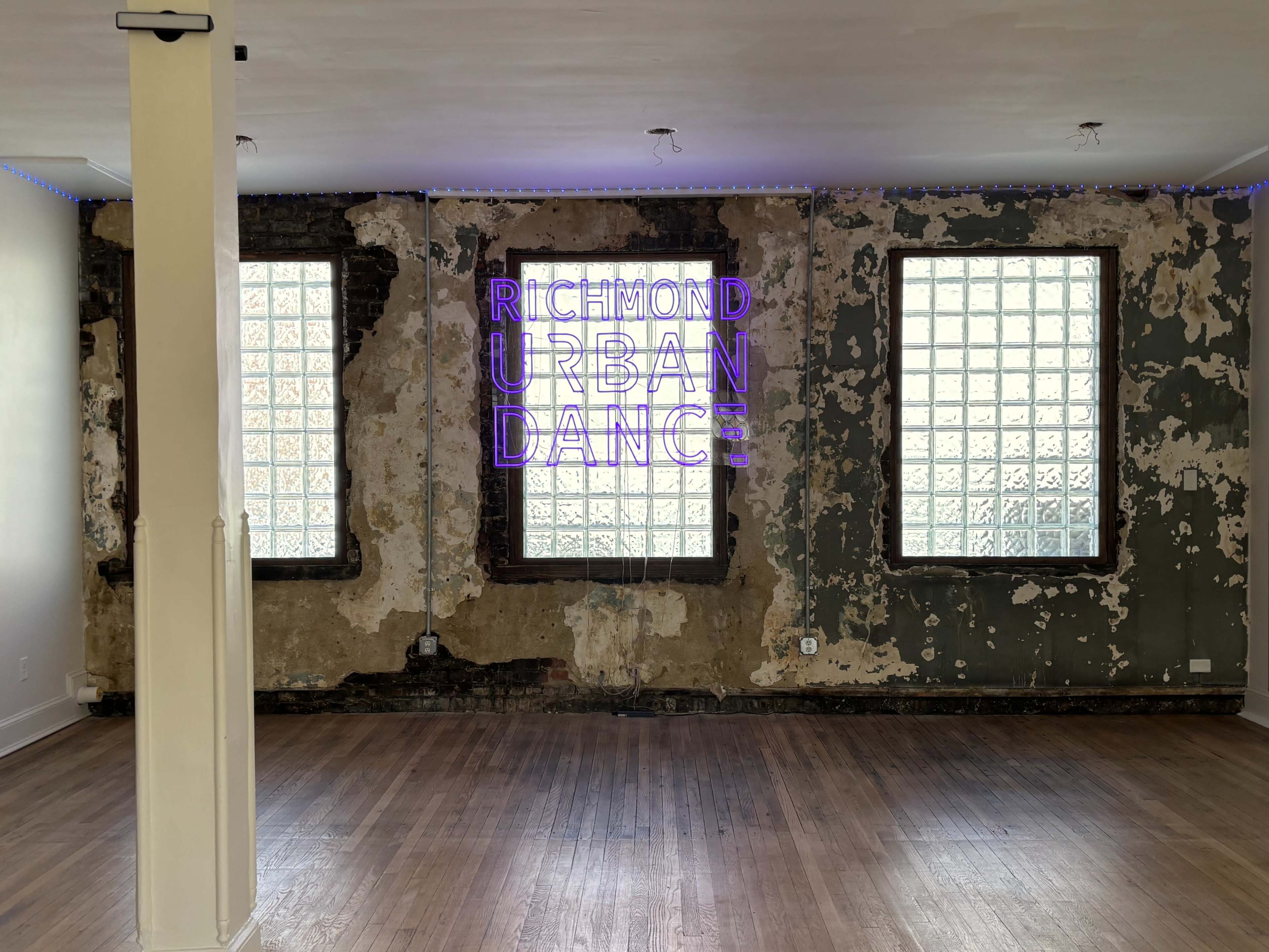 The image shows an interior space with a weathered wall, two glass block windows, and neon text reading "RICHMOND URBAN DANCE."