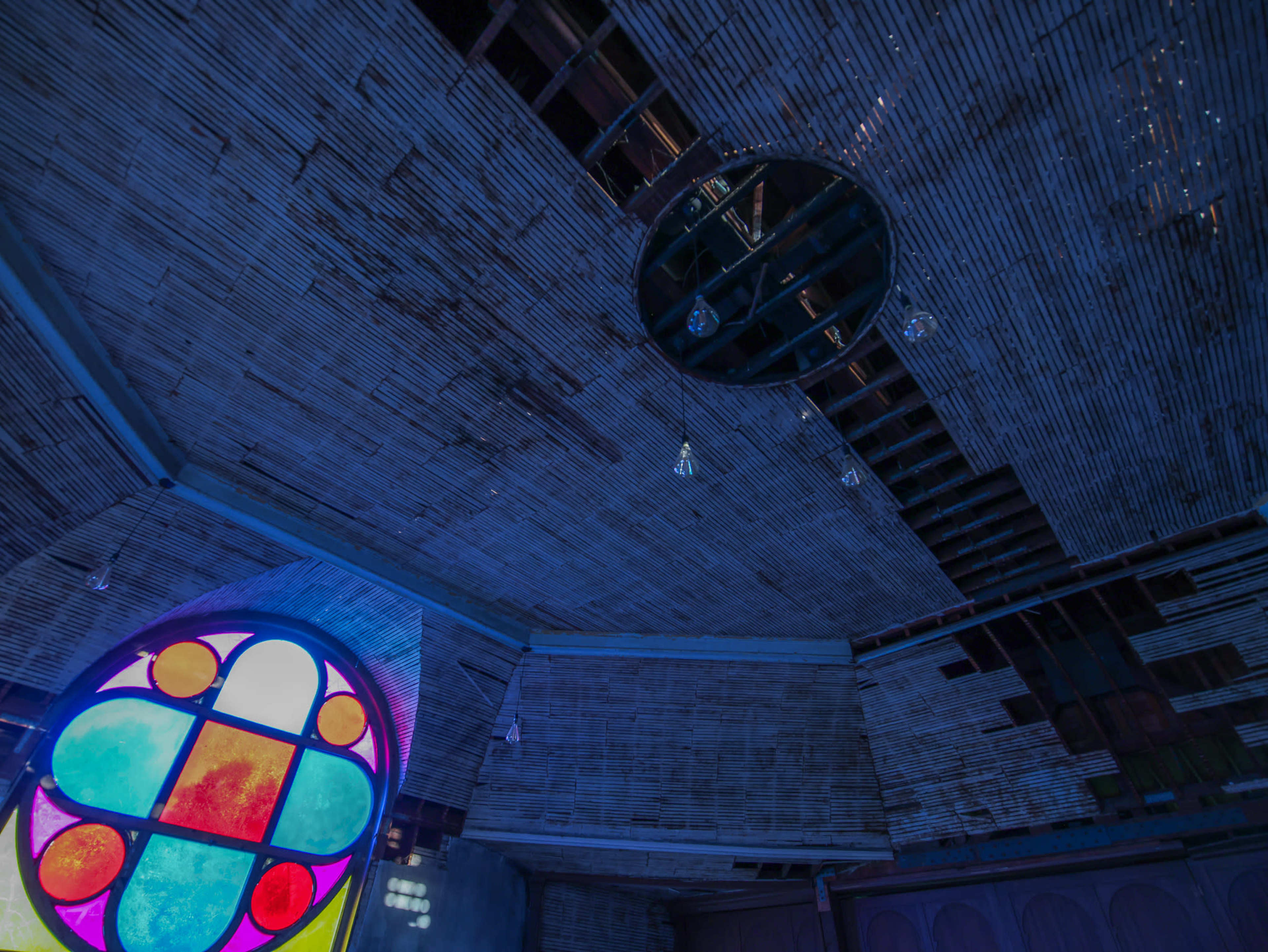 The interior of a building with a stained glass window displaying vibrant colors and a ceiling that features exposed beams and circular lights.
