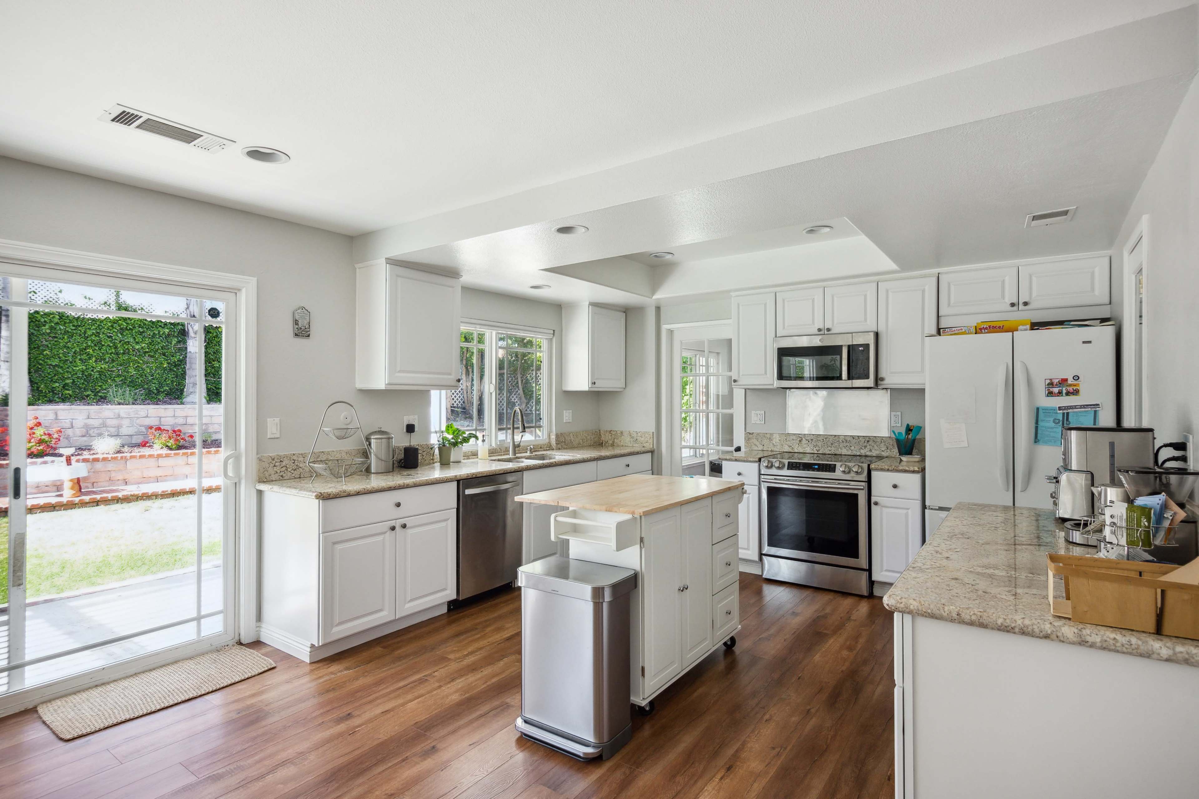 The kitchen features white cabinetry, stainless steel appliances, a central island, and a view of the backyard through sliding glass doors.