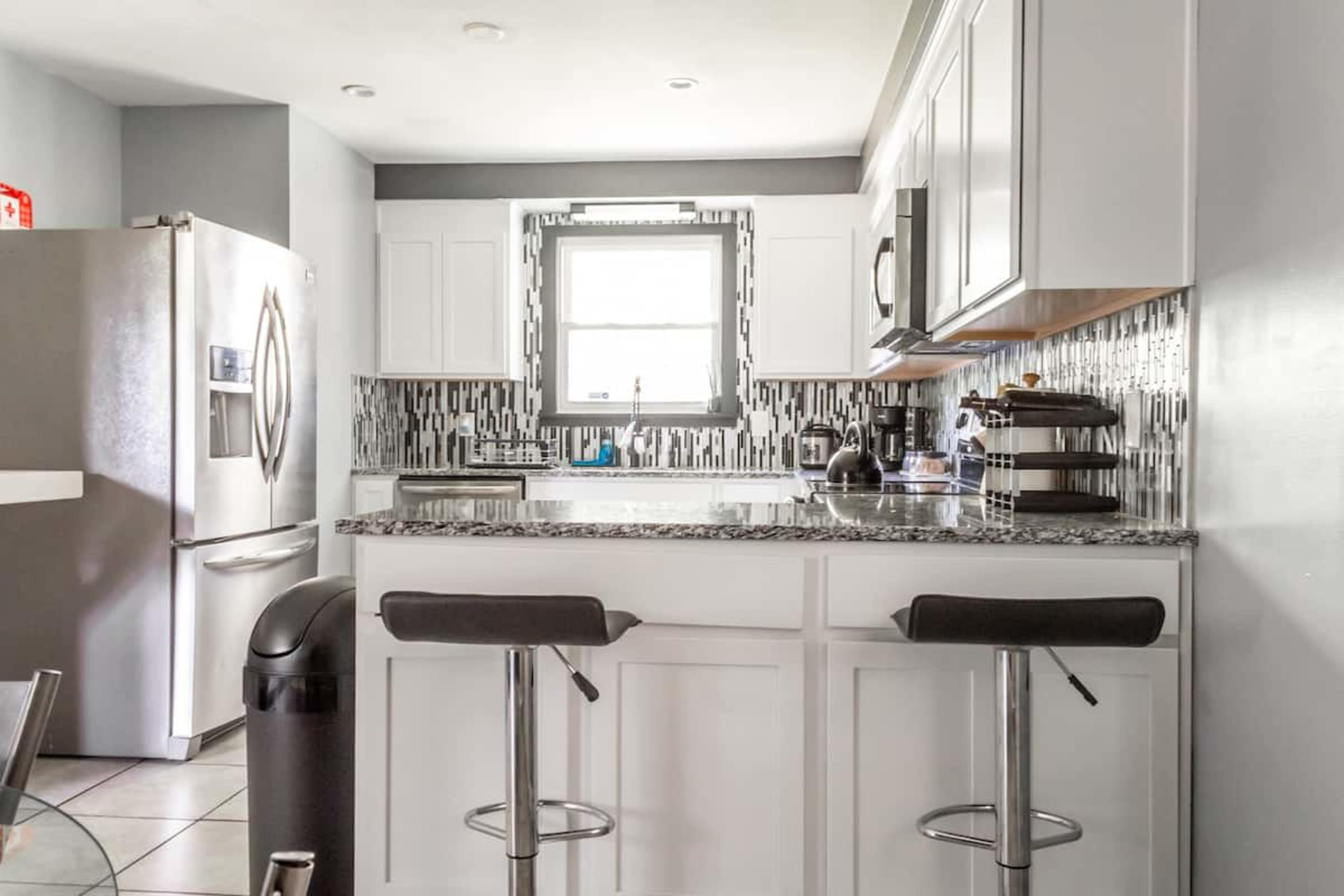 A modern kitchen features white cabinetry, a granite countertop, stainless steel appliances, and a tiled backsplash.
