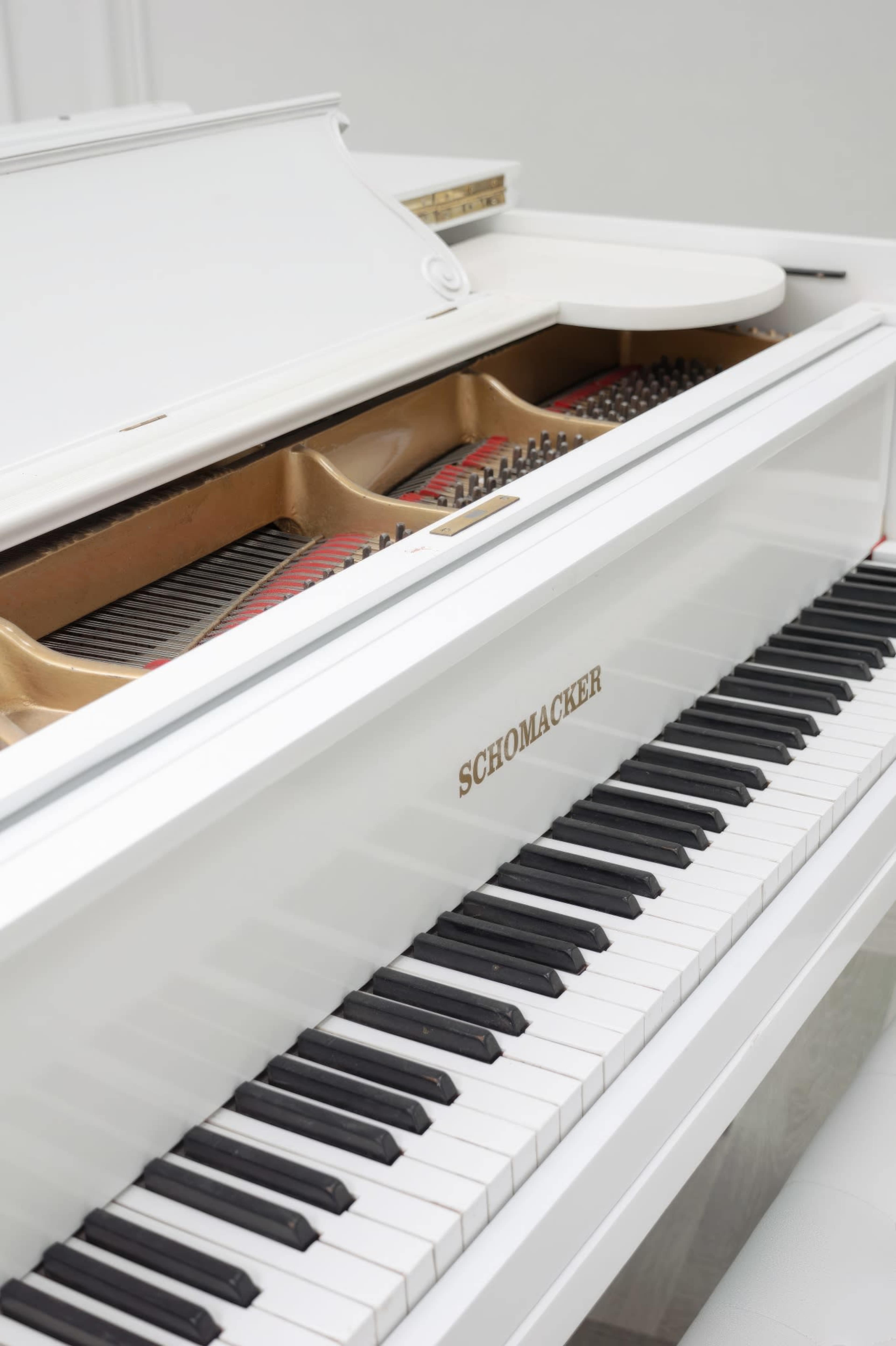 A white piano with the brand name "Schoenacker" visible on its front, featuring a polished surface and open lid that reveals the strings inside.