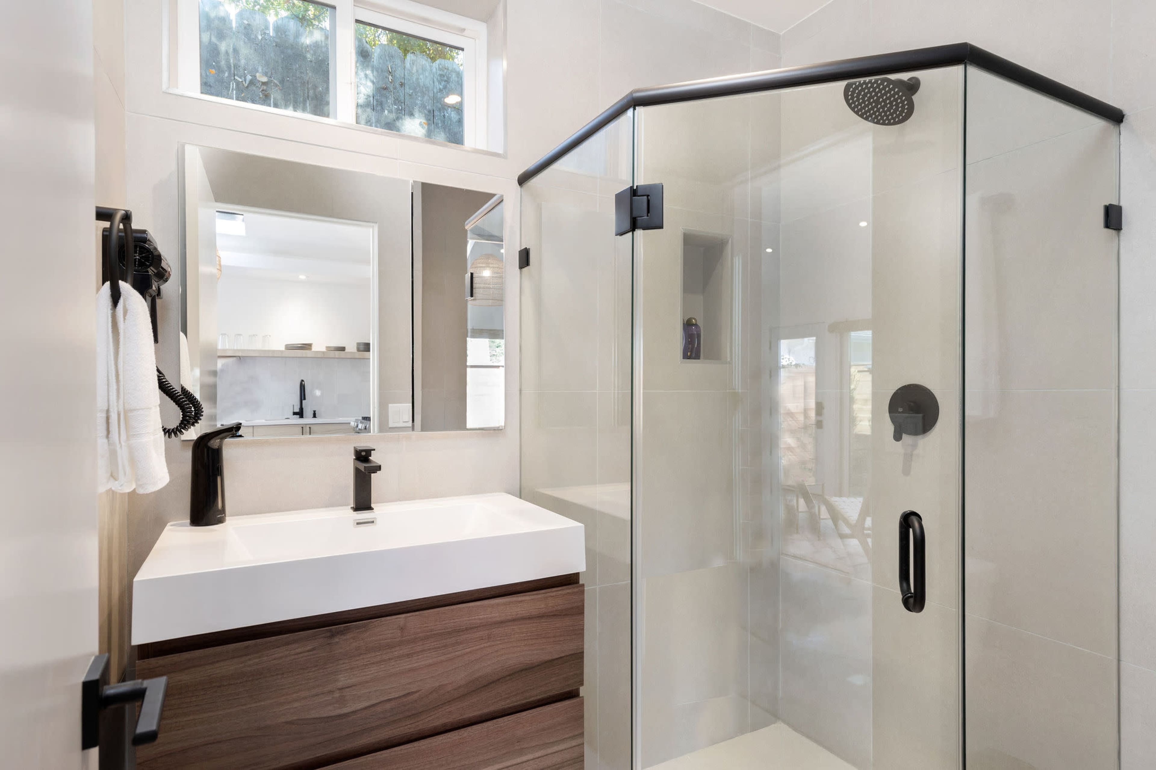 A modern bathroom with a glass shower, a sleek sink on a wooden vanity, and a large mirror reflecting the space.