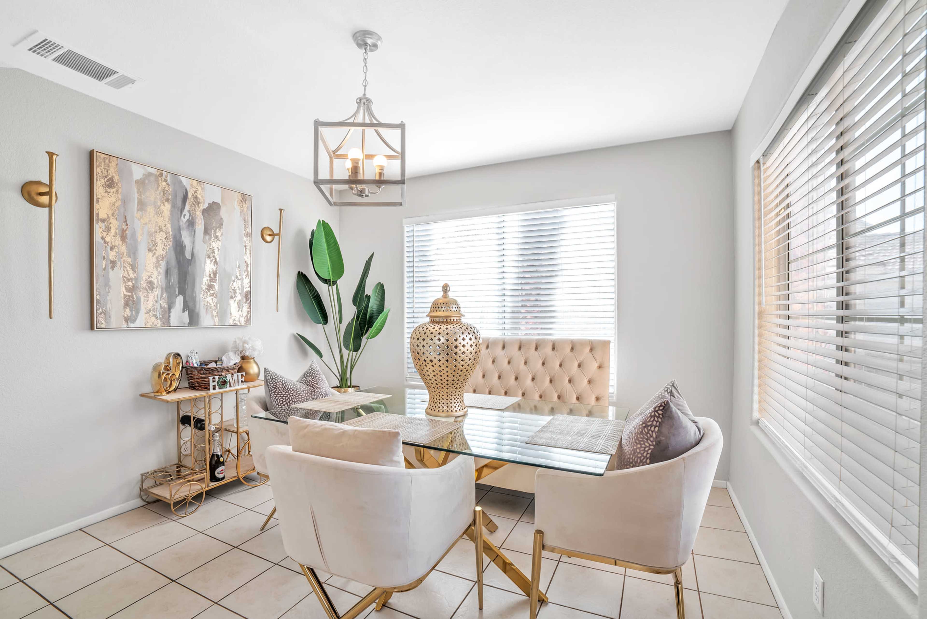 A modern dining area features a glass table surrounded by beige upholstered chairs, with a large decorative vase and a potted plant in the corner.