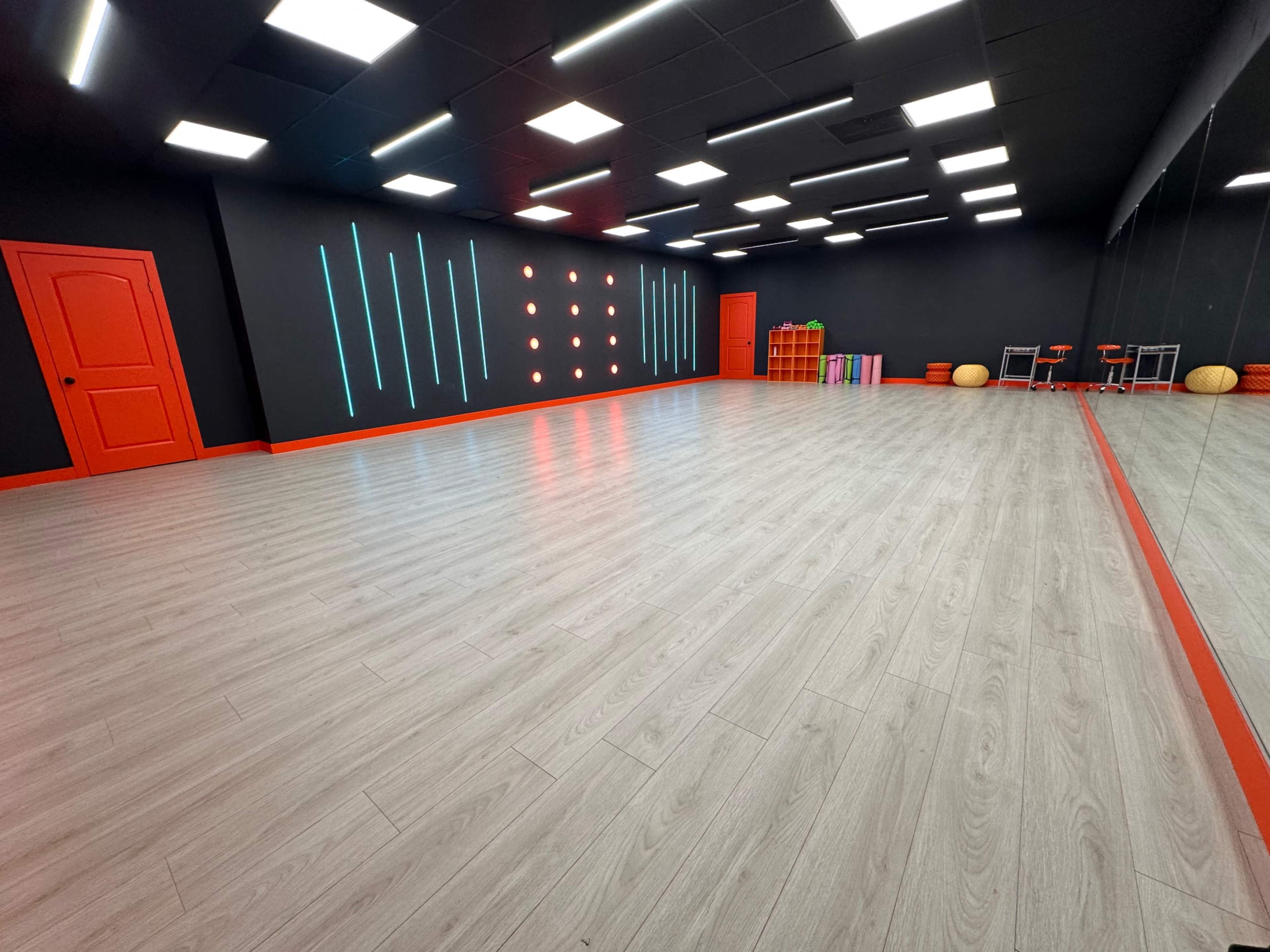 A brightly lit exercise studio with a wooden floor, black walls, and colorful accents, including a red door and vibrant wall decorations.