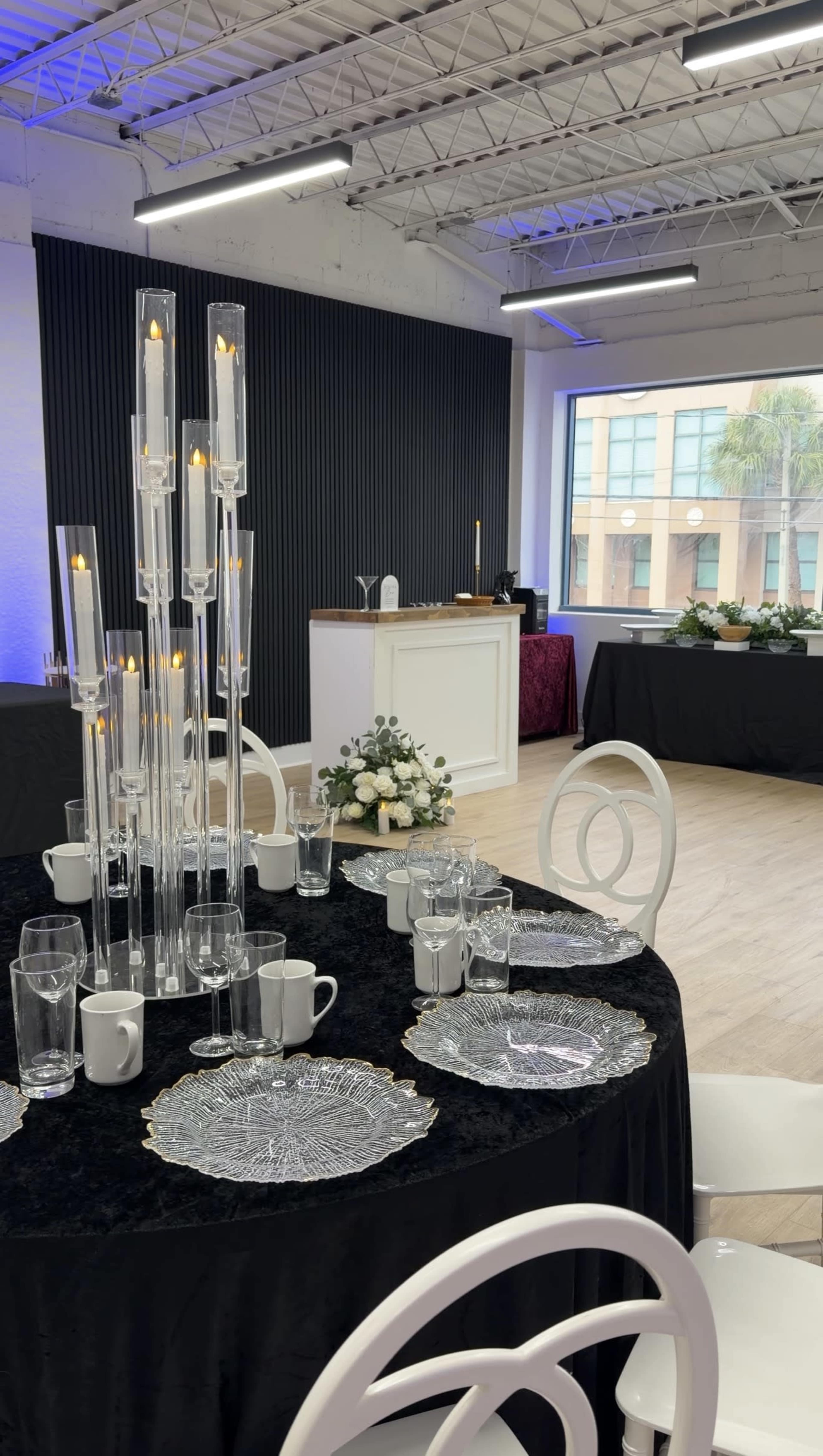 A dining table set with elegant dishware and a tall centerpiece of glass candlesticks is arranged in a well-lit, modern event space.