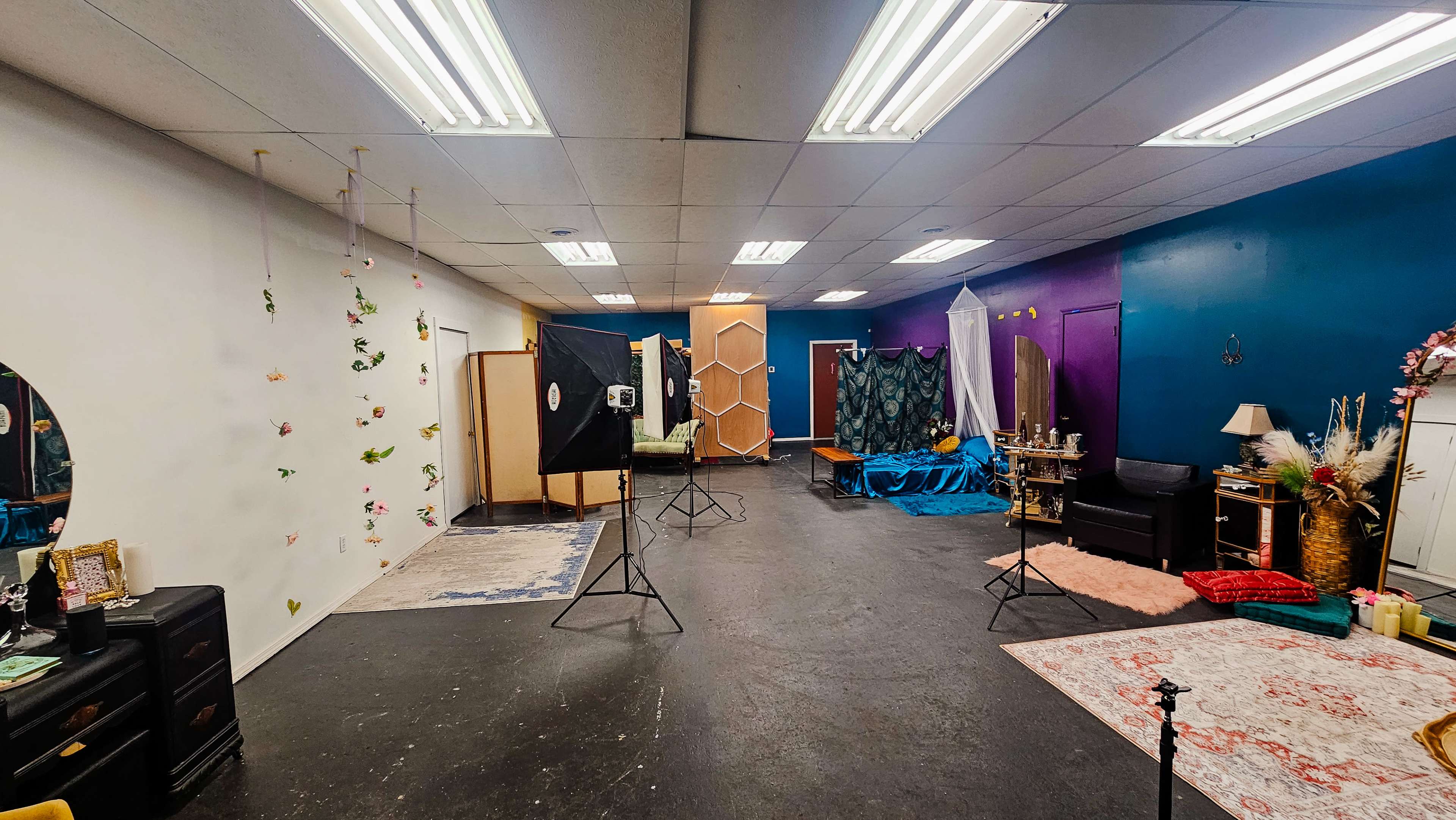 The image shows a spacious photography studio with various backdrops, lighting equipment, and a mix of decorative elements arranged around the room.