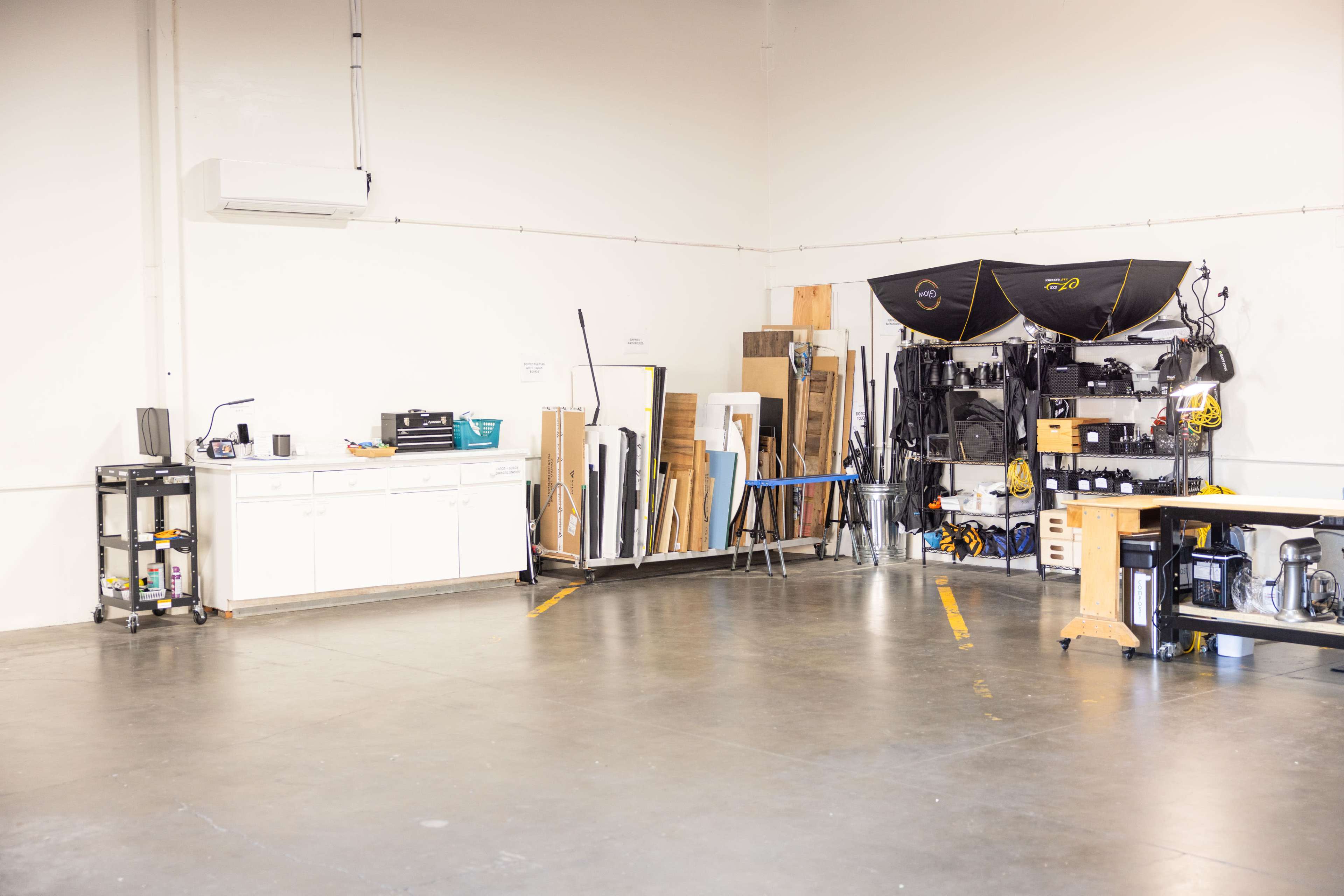 The image shows a spacious workshop area with a kitchenette on one side and various tools and materials neatly organized along the wall.