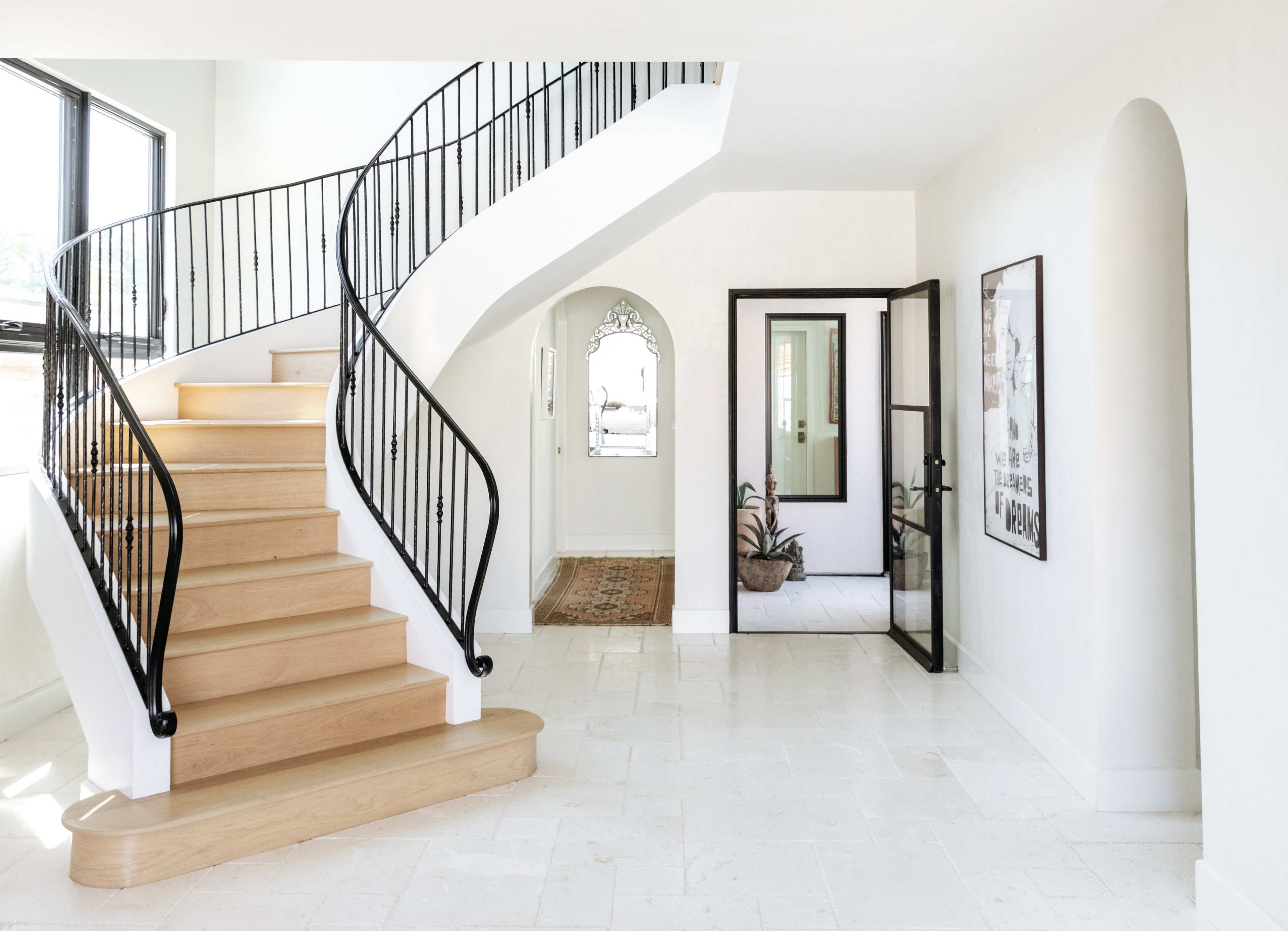 A spacious foyer with a curved wooden staircase, a black wrought iron railing, and a doorway leading to another room.