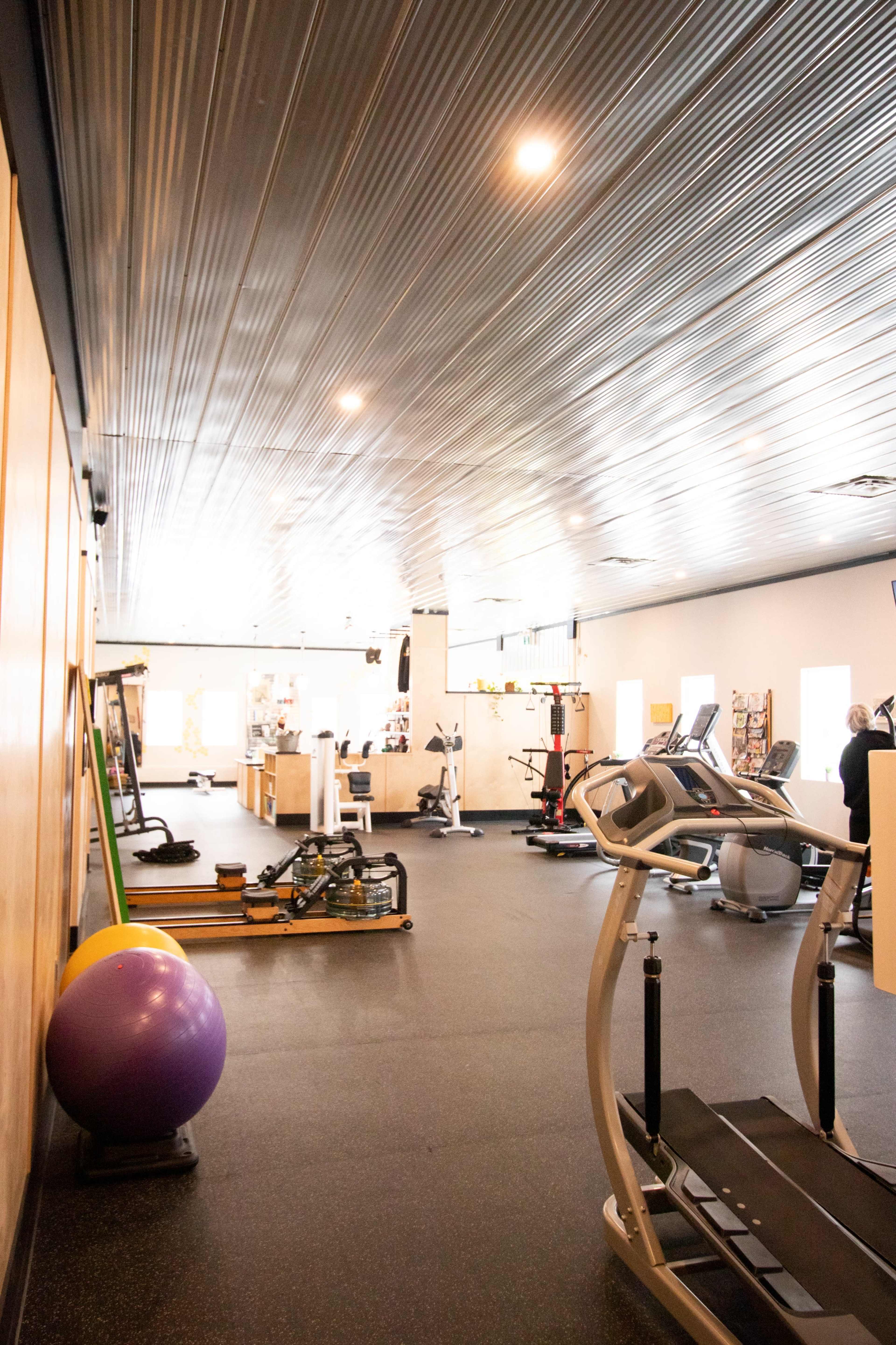 An interior view of a fitness gym with various exercise equipment, including a treadmill, weights, and a large exercise ball.