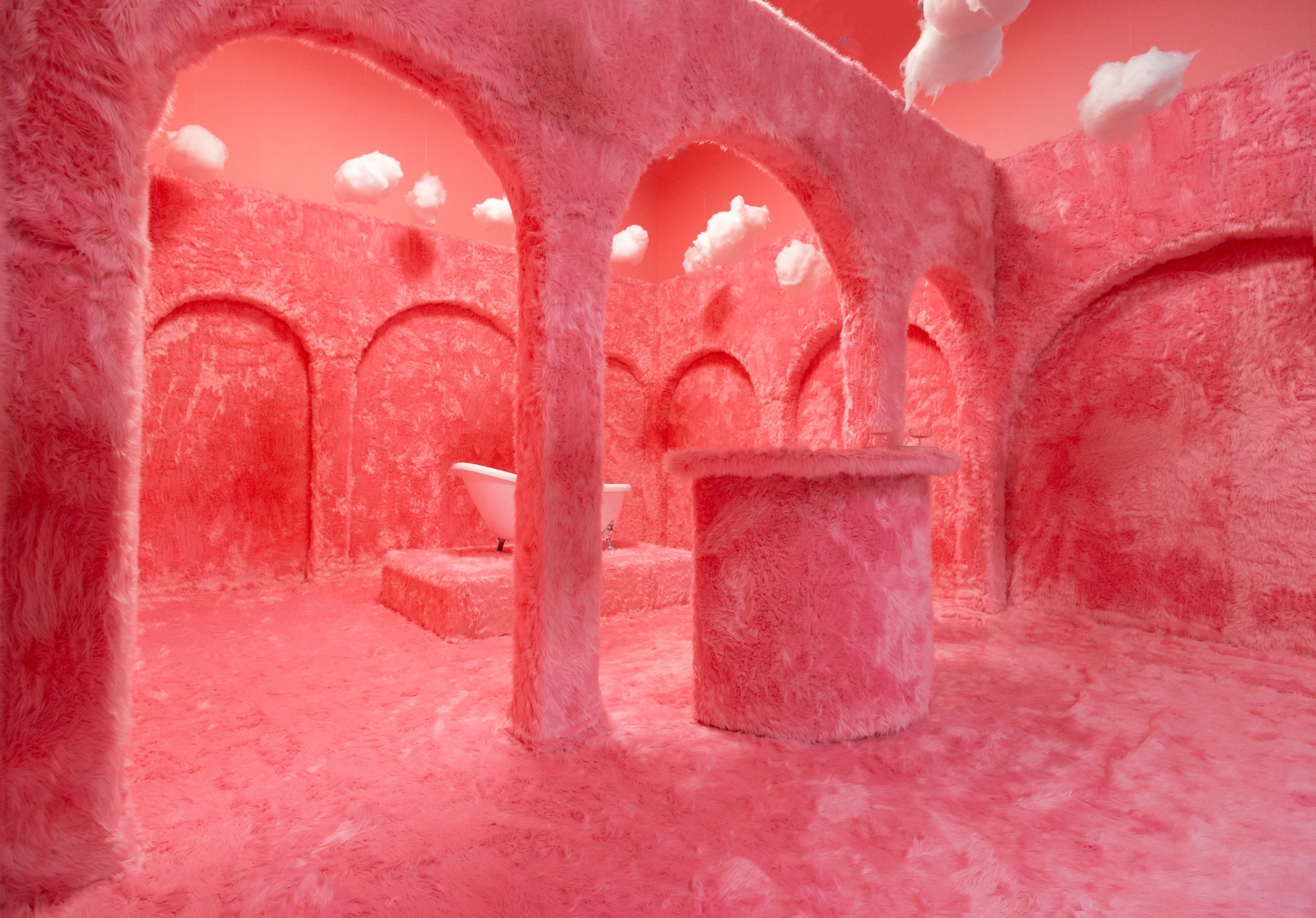 The image shows a surreal pink room with textured walls and arches, featuring a bathtub on a raised platform and fluffy clouds suspended from the ceiling.