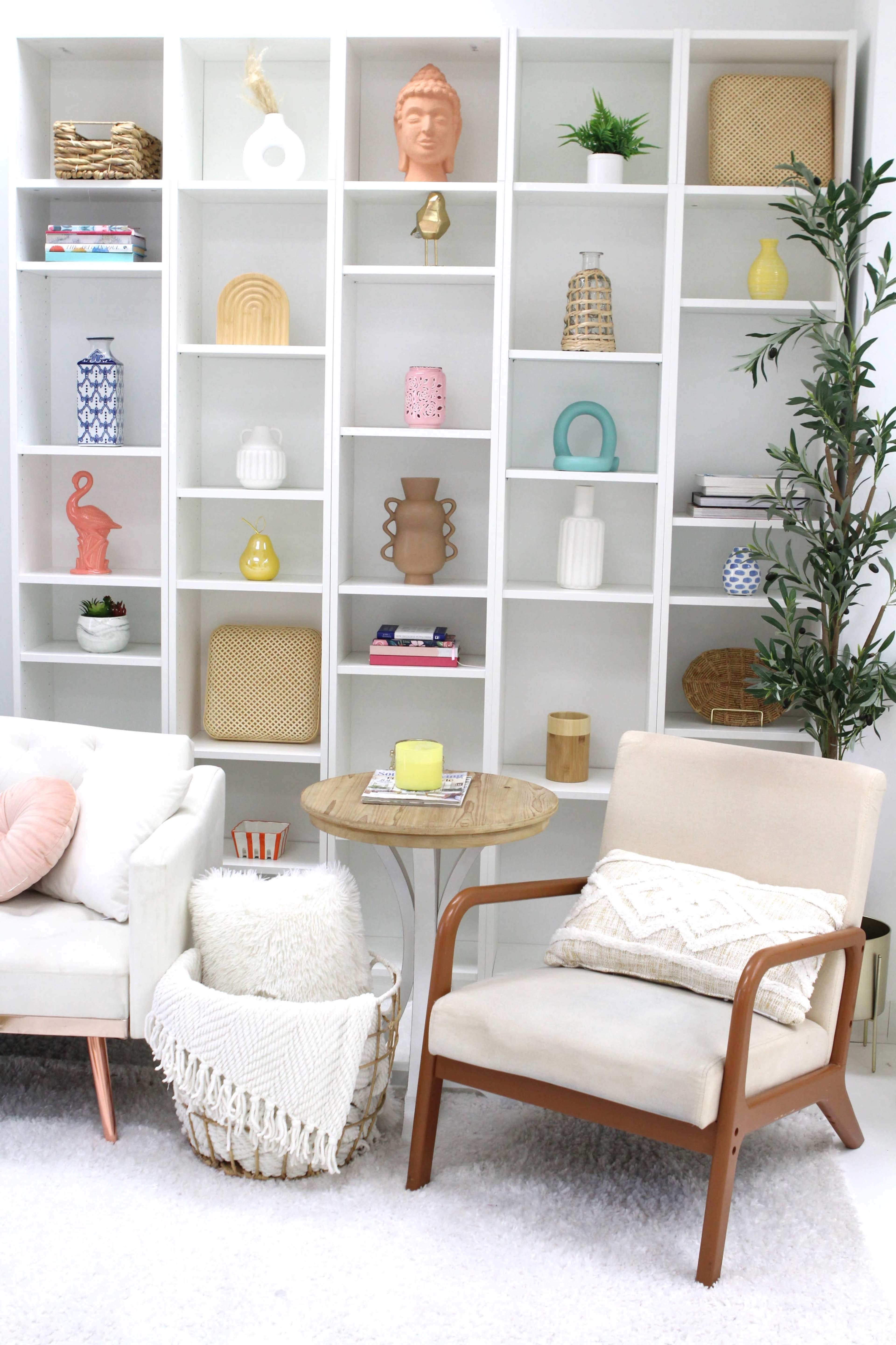 A white shelving unit displays decorative items alongside a beige armchair and a small table in a living room setting.