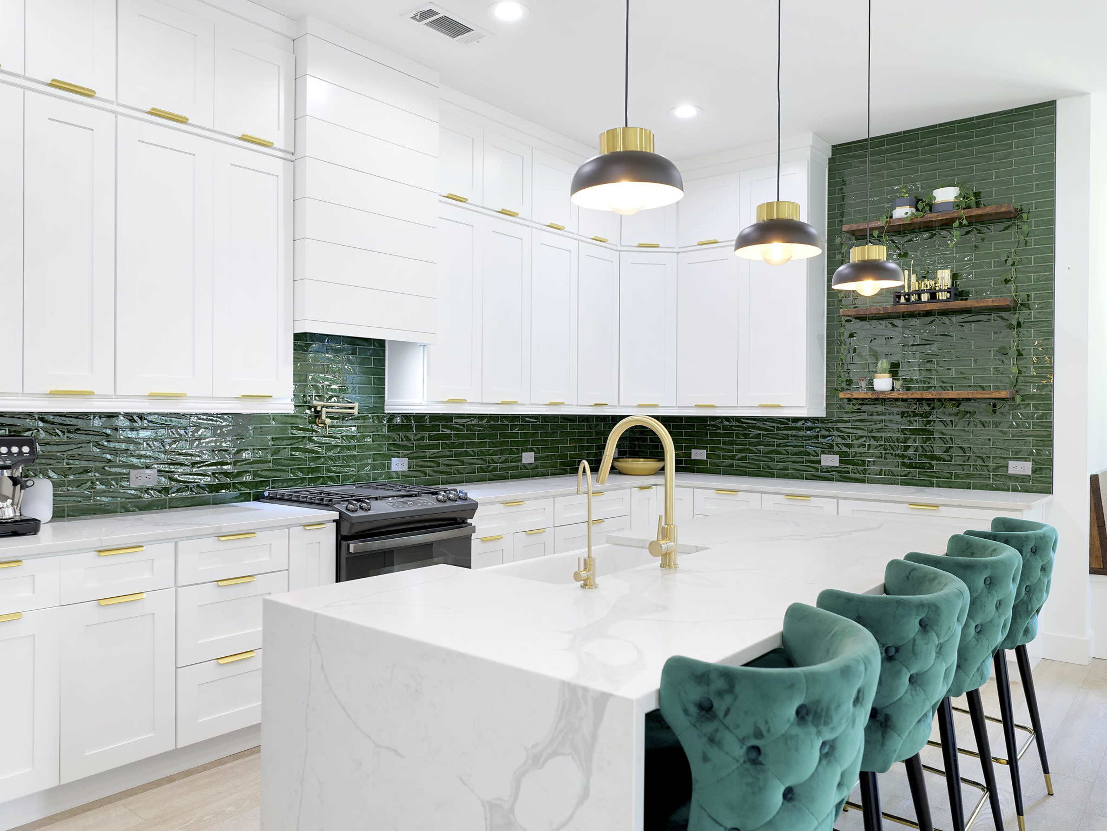 The kitchen features white cabinetry, a green tiled backsplash, a marble countertop, and teal bar stools.