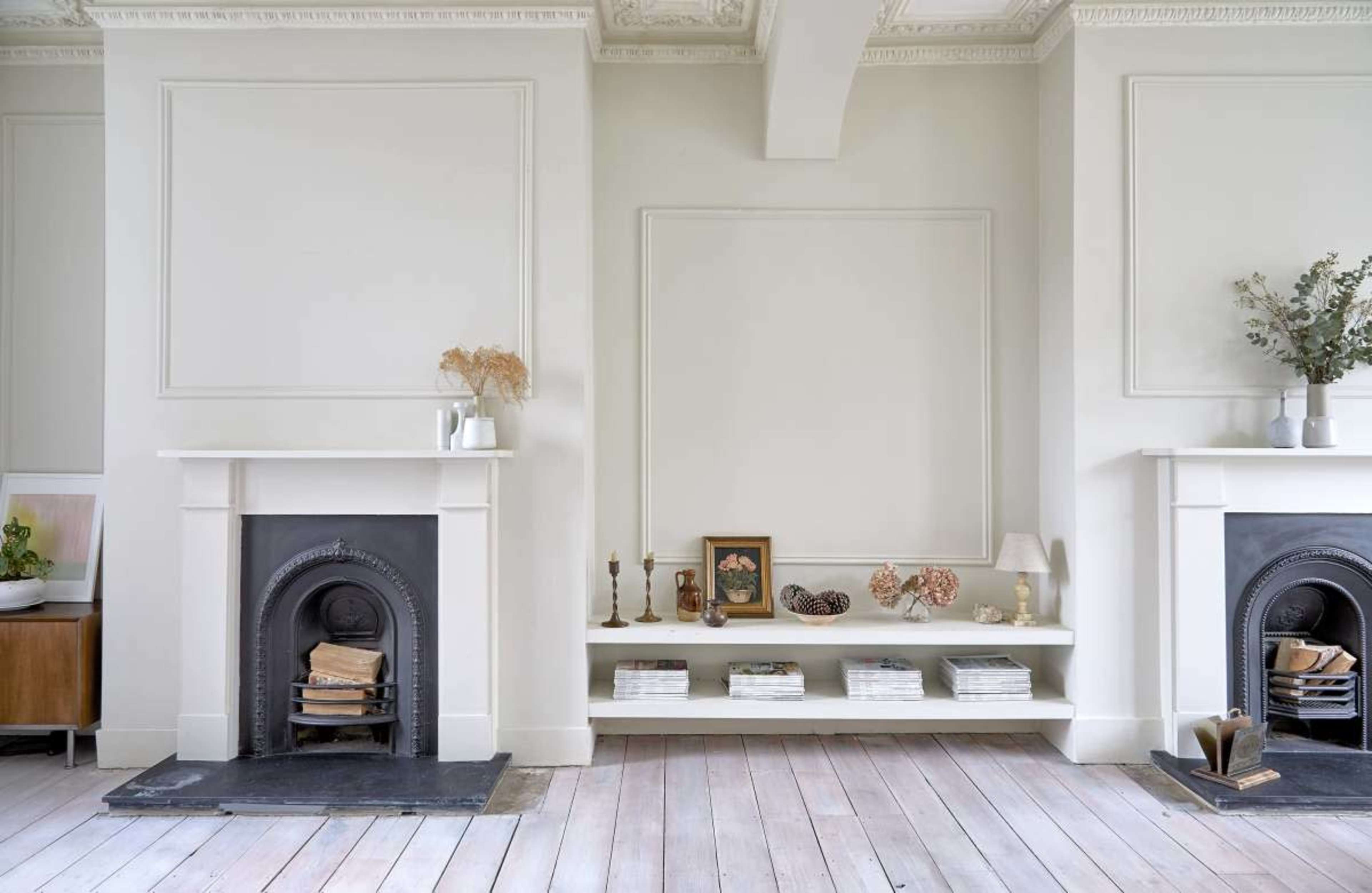 The image features a minimalist interior with two fireplace mantels flanking a central shelf, both adorned with decorative items and arranged books.