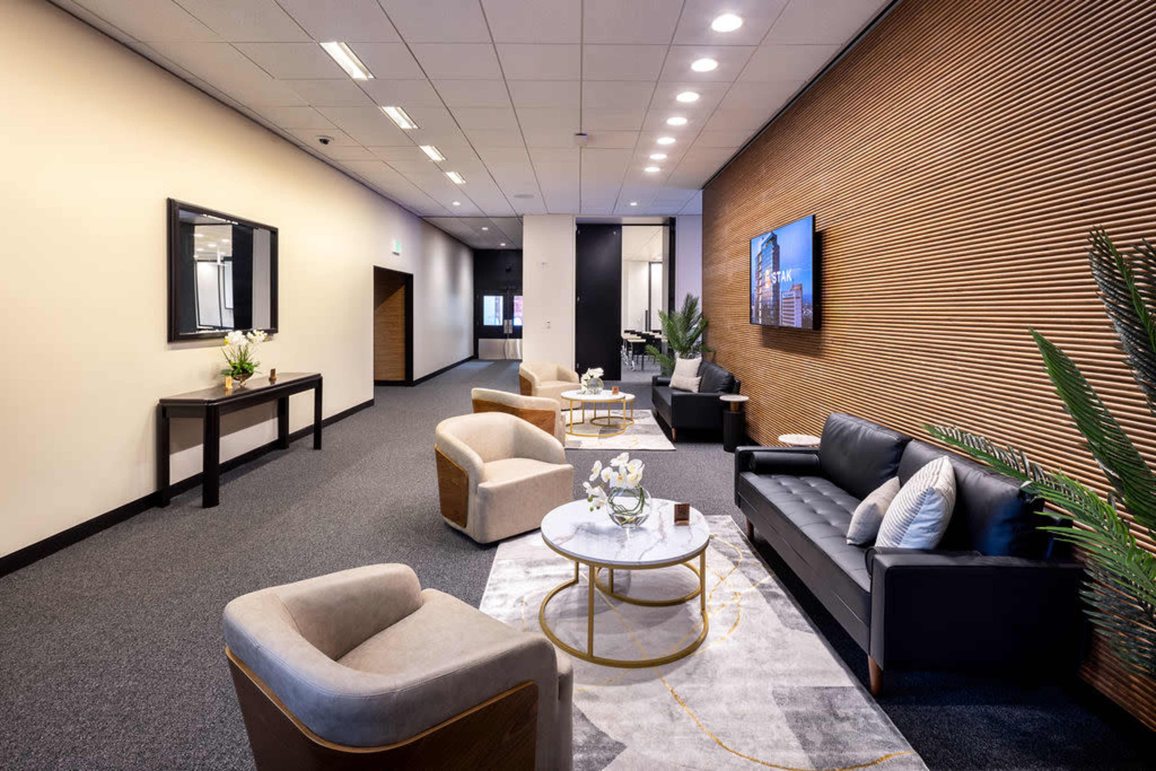 The image shows a modern waiting area with a seating arrangement that includes a black couch, two cream-colored armchairs, and a round coffee table, complemented by wall decor and plants.