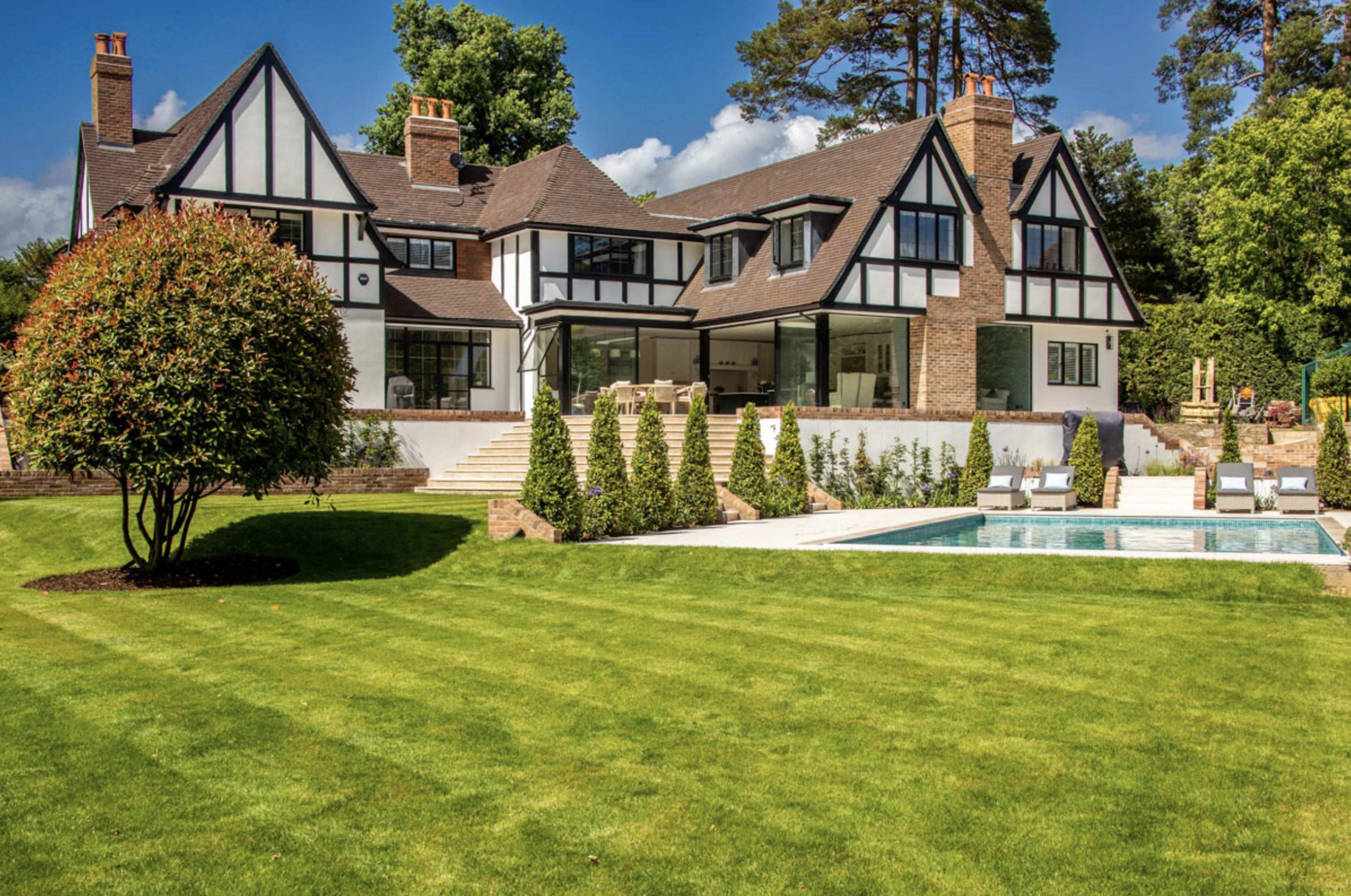 A large, two-story house with a distinct architectural style and a swimming pool surrounded by a well-maintained lawn.