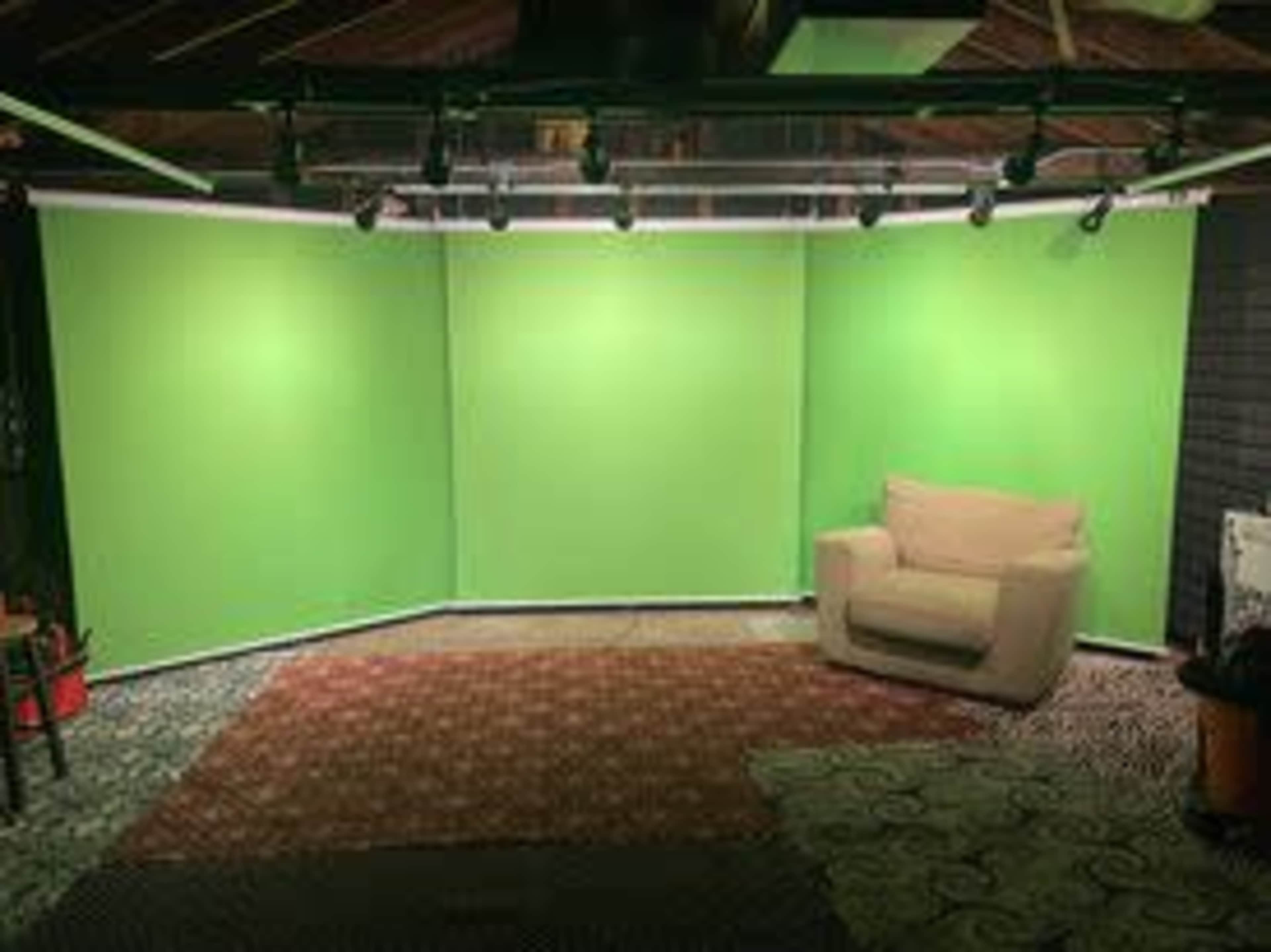 A room with three green screens arranged in a corner and a beige couch placed on a patterned rug.