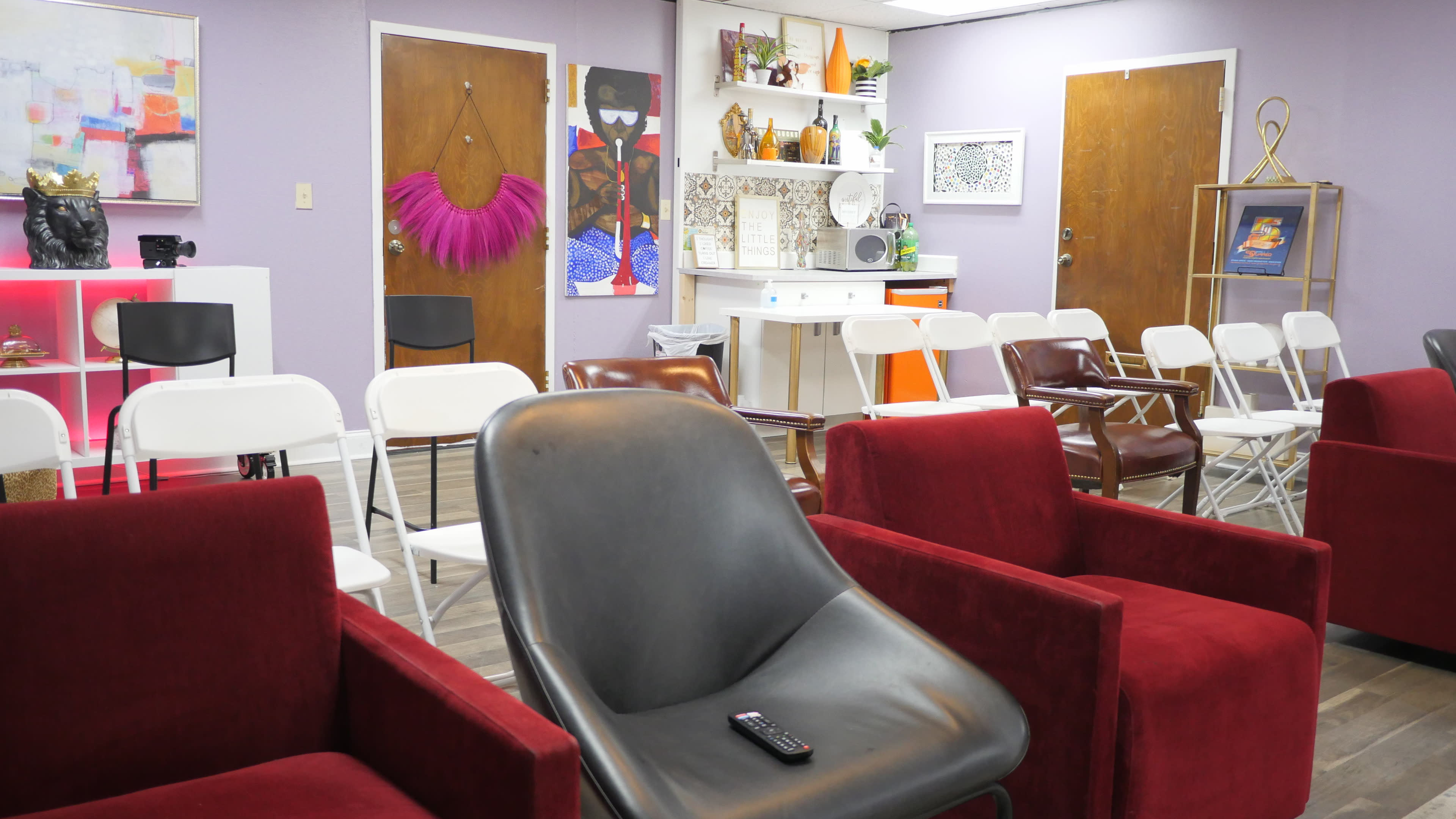 A waiting area with several empty chairs arranged in rows, featuring a mix of red and black armchairs, and colorful wall decorations.