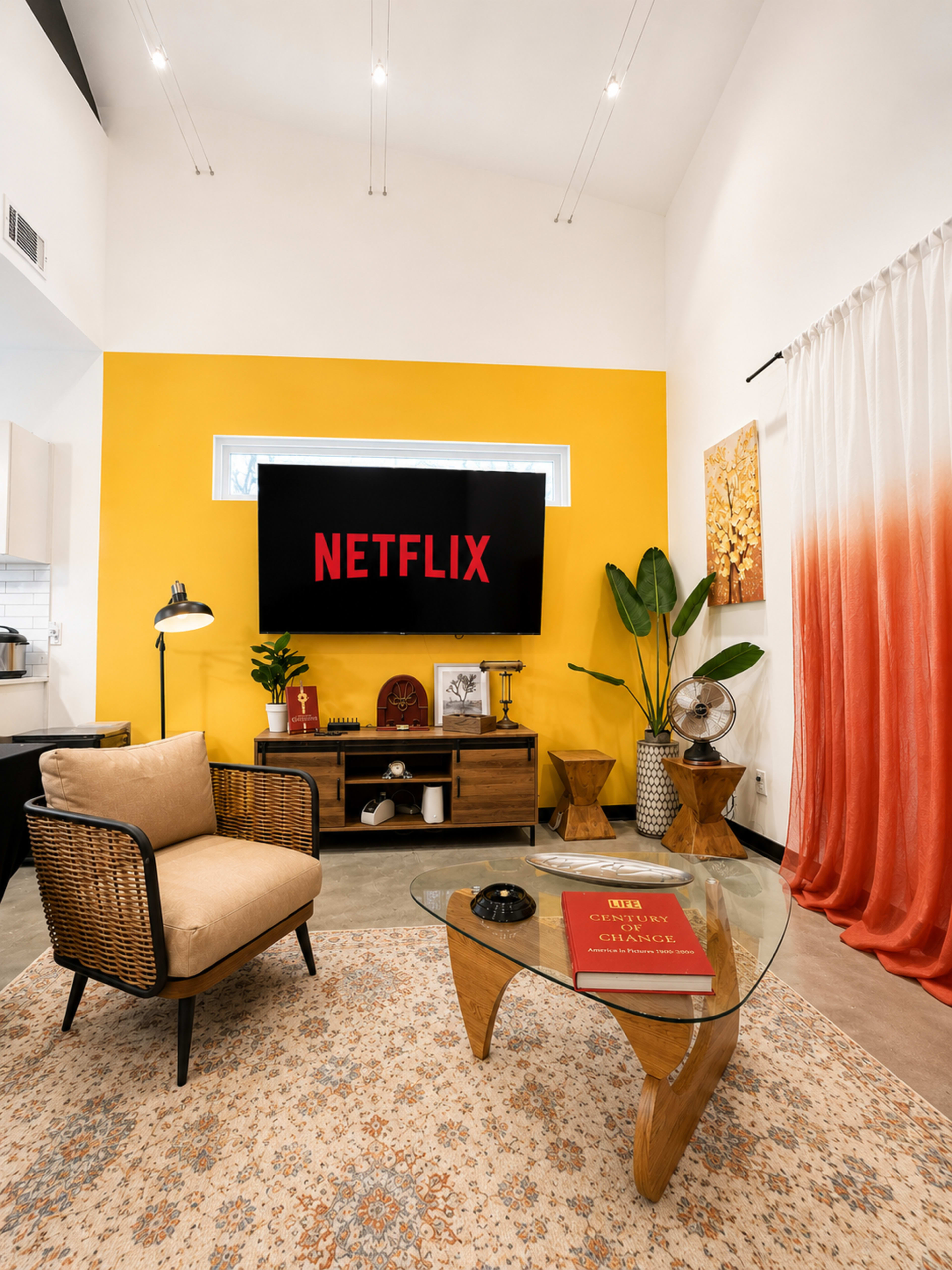 The image shows a modern living room with a yellow accent wall, featuring a Netflix screen on display, a stylish armchair, a glass coffee table, and decorative elements.