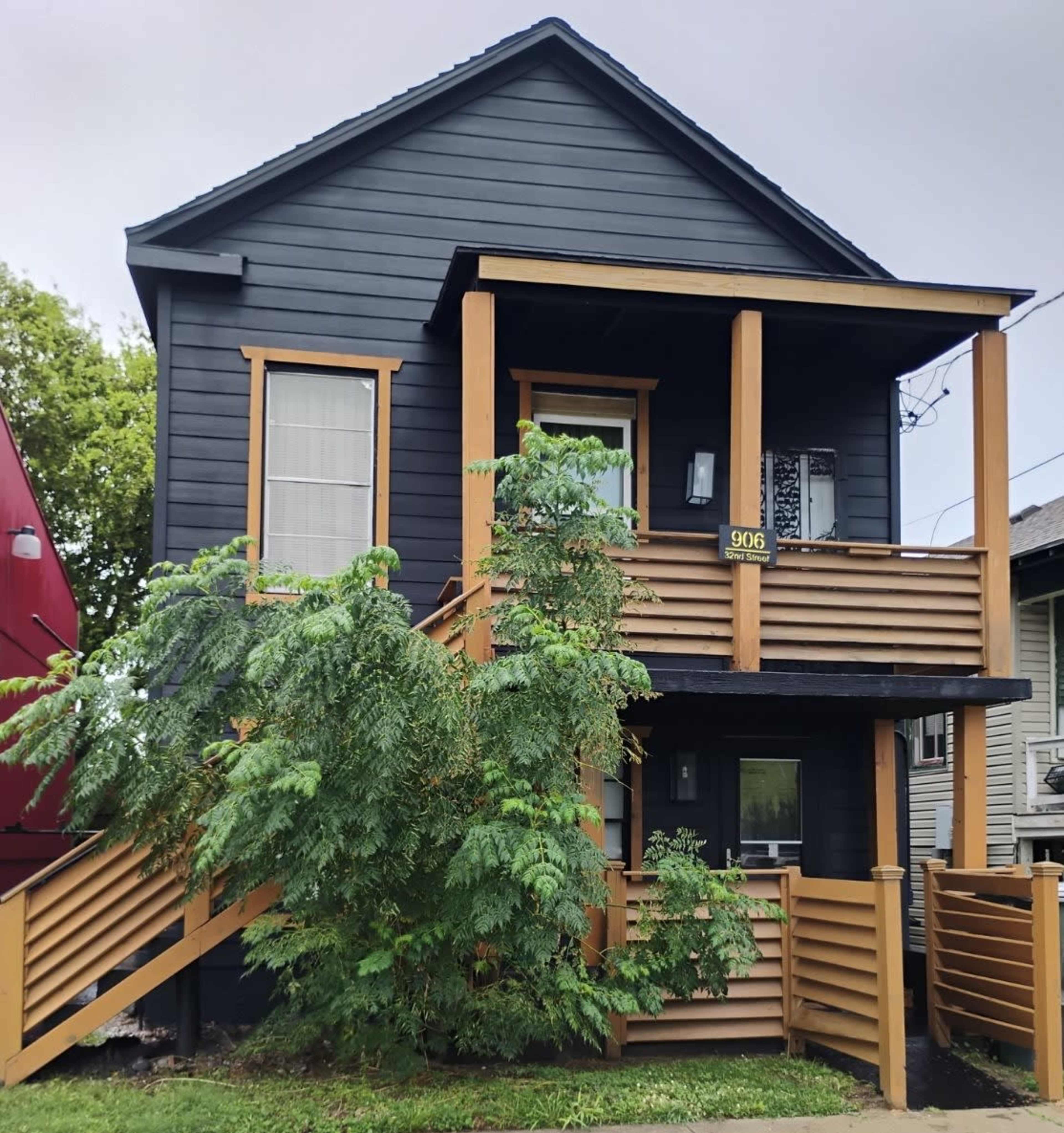 A two-story black house features wooden accents and a front porch with steps leading up to the entrance.