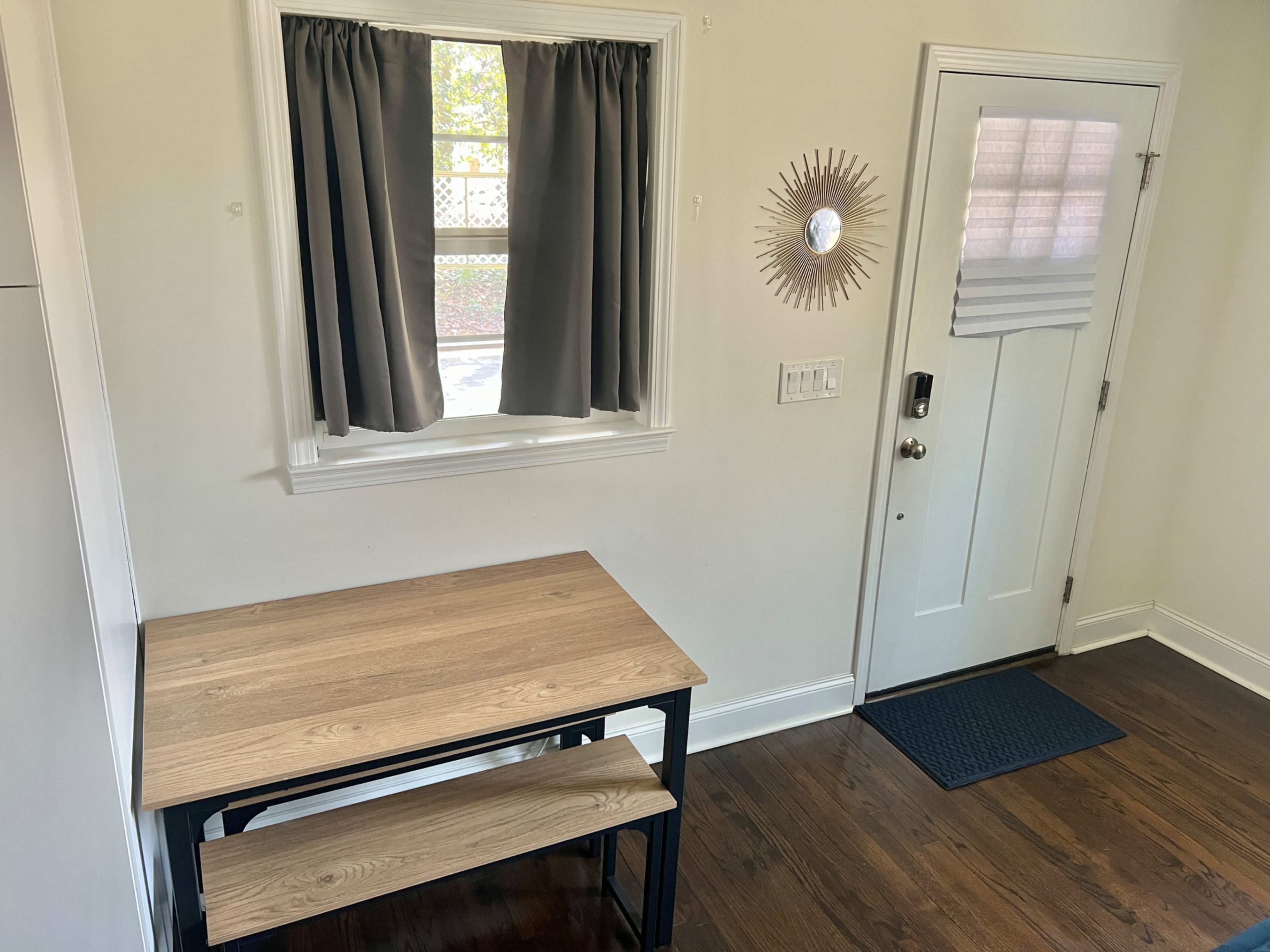 A small dining area with a wooden table and benches next to a door and a window with gray curtains.