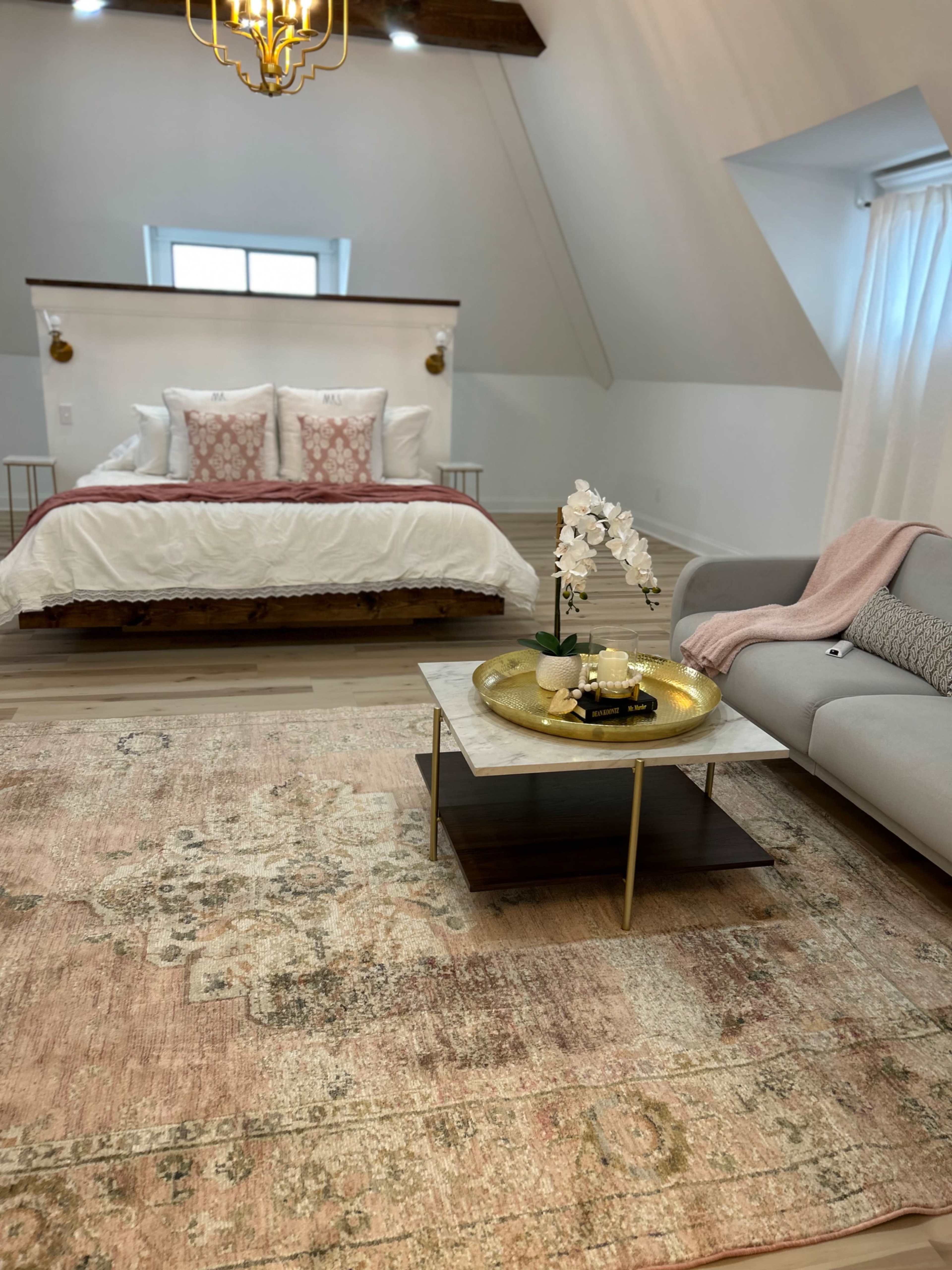 A modern bedroom featuring a large bed with decorative pillows, a coffee table with a decorative tray, and a plush area rug on a wooden floor.
