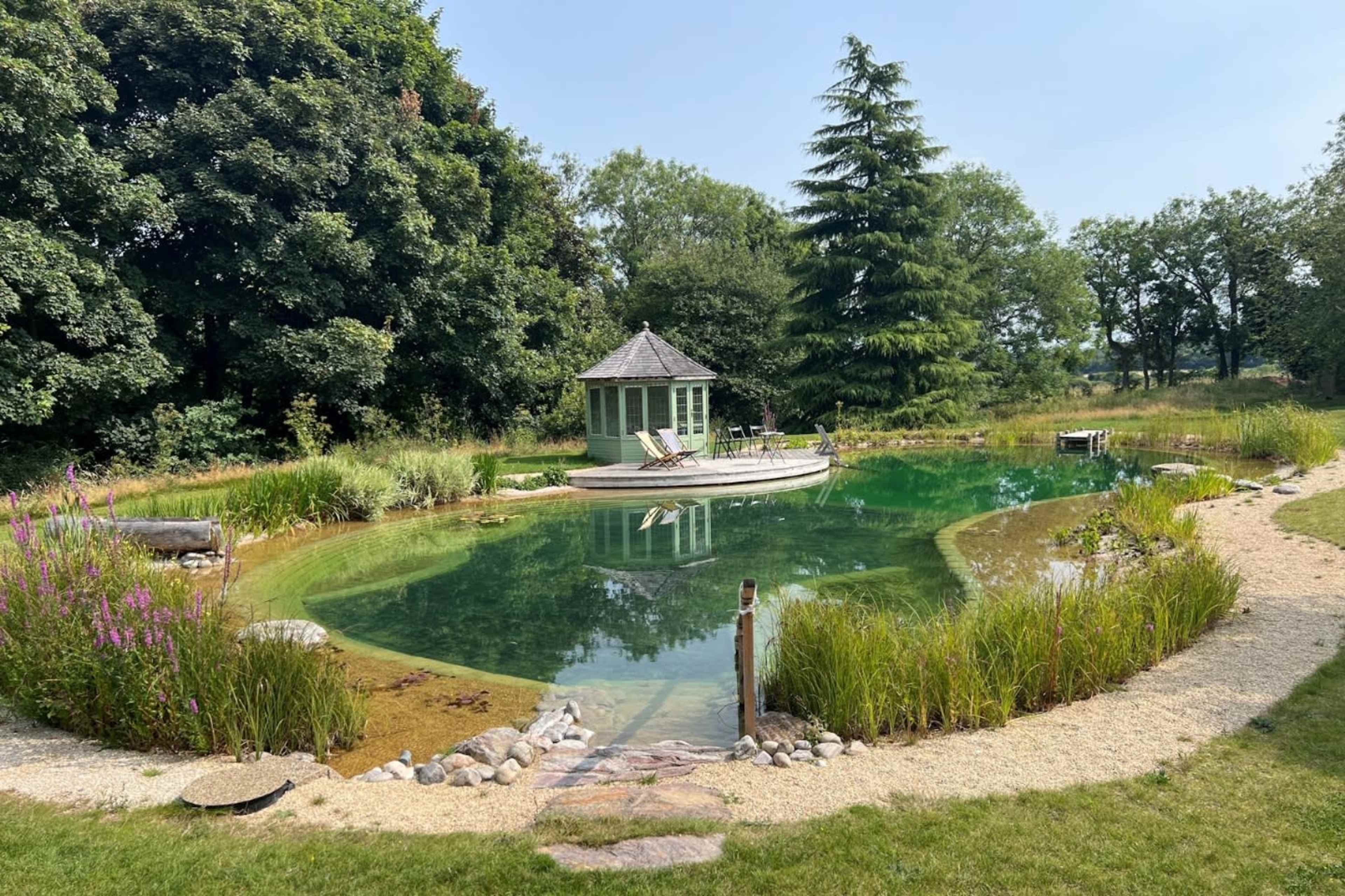 A circular pond surrounded by greenery features a small gazebo on a raised platform at its center.