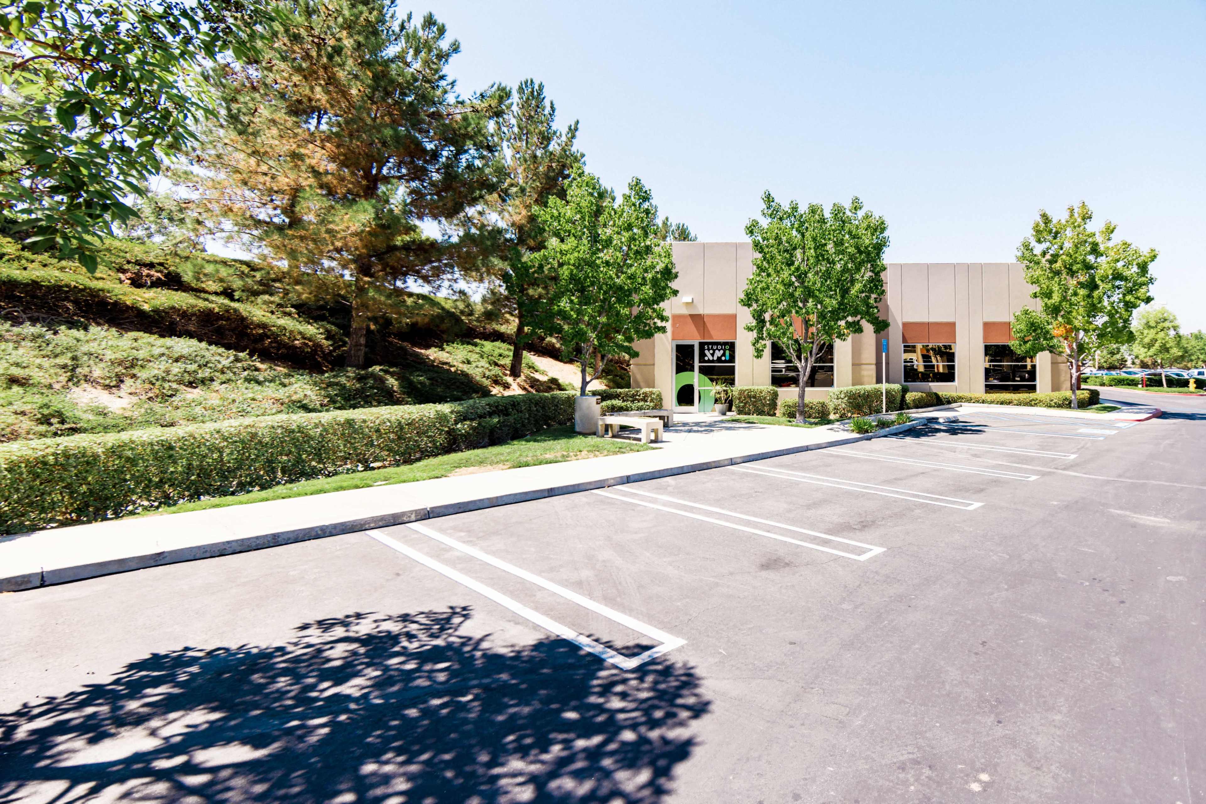 A vacant parking lot in front of a commercial building surrounded by manicured bushes and trees.