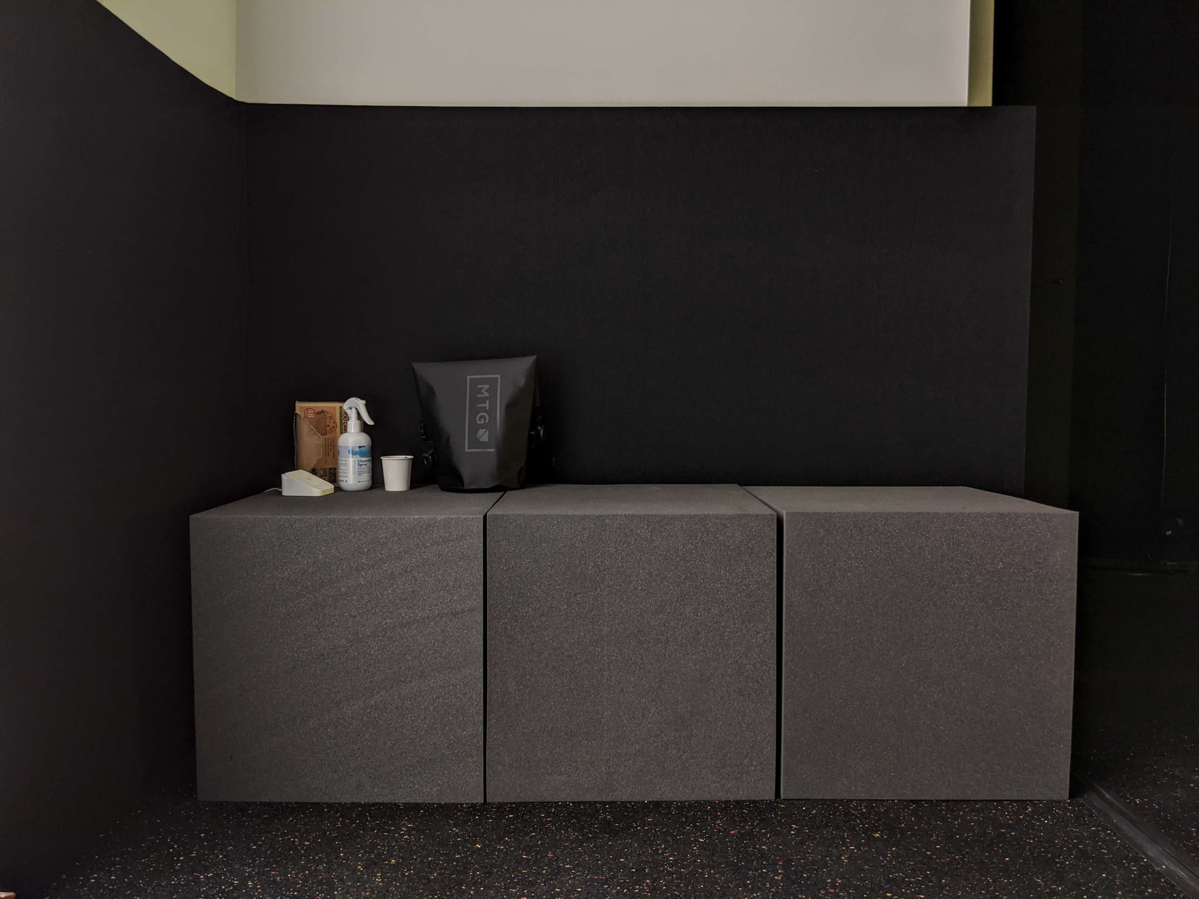 A minimalist black corner features three gray storage cubes alongside a small arrangement of items, including a spray bottle and a bag.