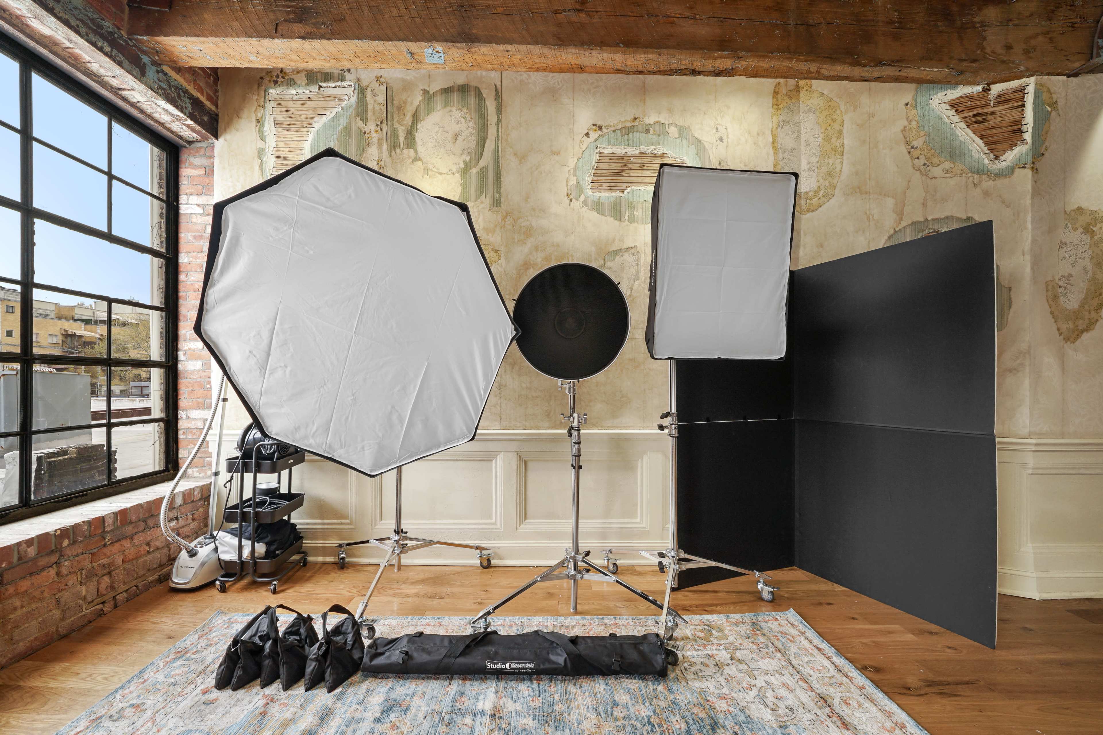 A photography setup featuring softbox lights and a reflector in a room with exposed brick walls and large windows.