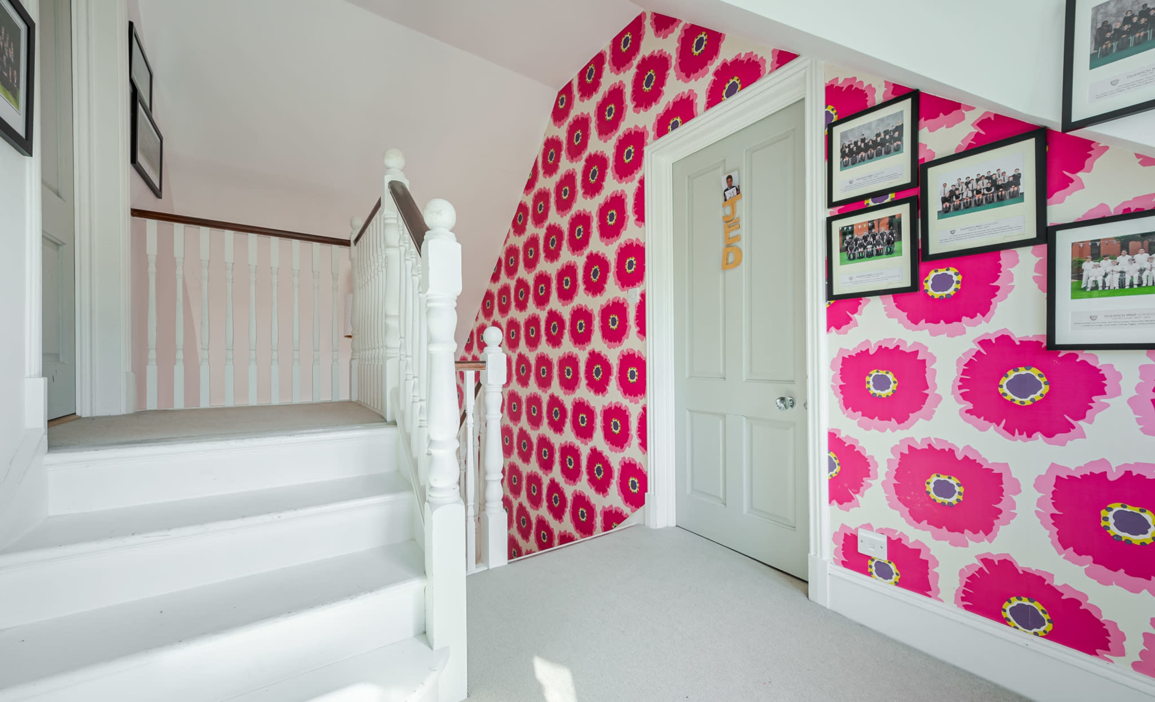 A staircase leads to a hallway with bright floral wallpaper and framed pictures on the walls.