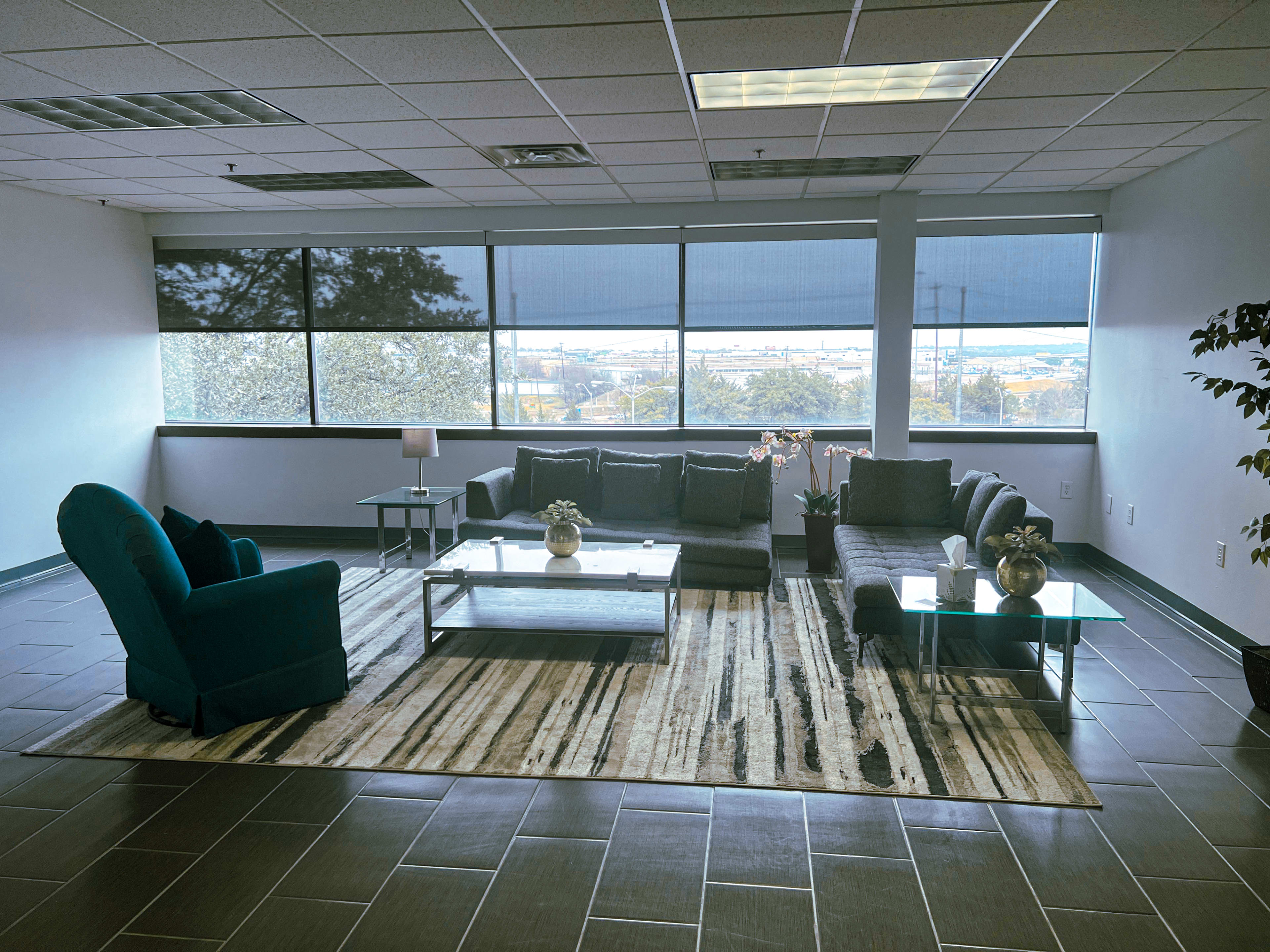 A modern lounge area features a mix of seating arrangements, a coffee table, and large windows with a view of the outside.