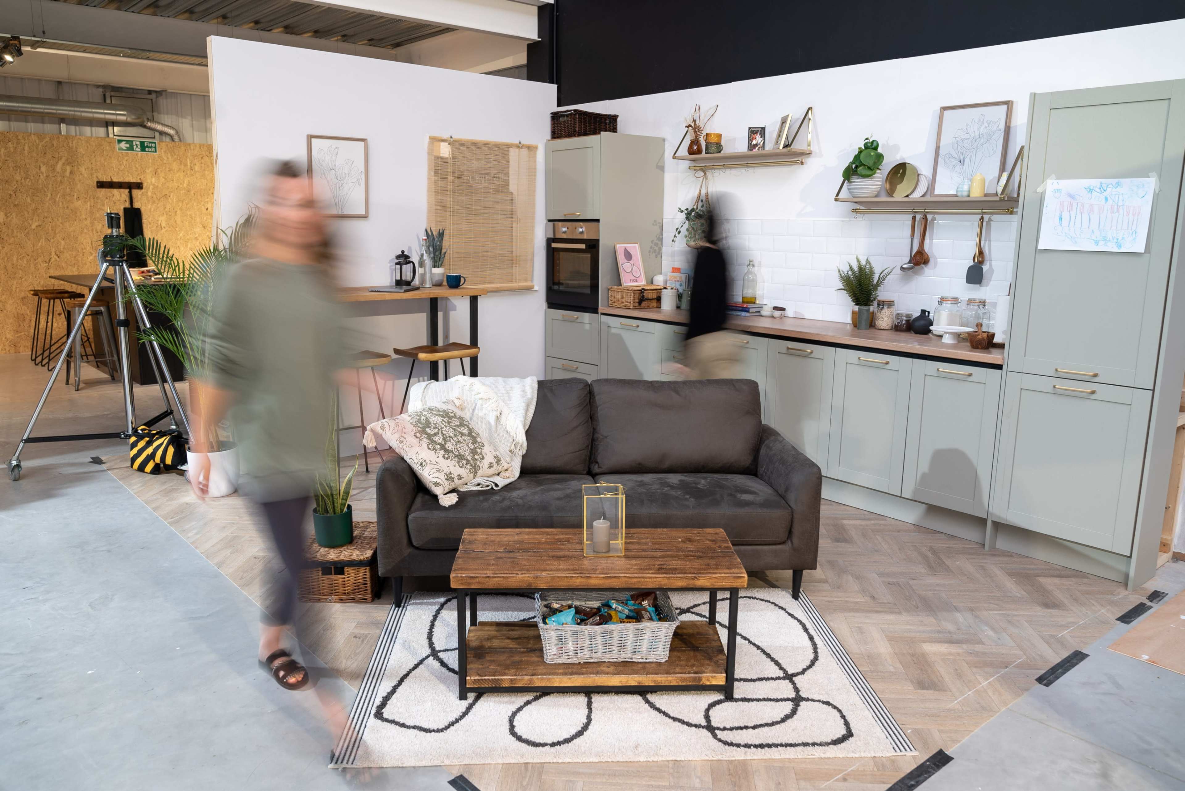 The image shows a modern living space with a kitchen and a cozy seating area featuring a dark sofa and a wooden coffee table.