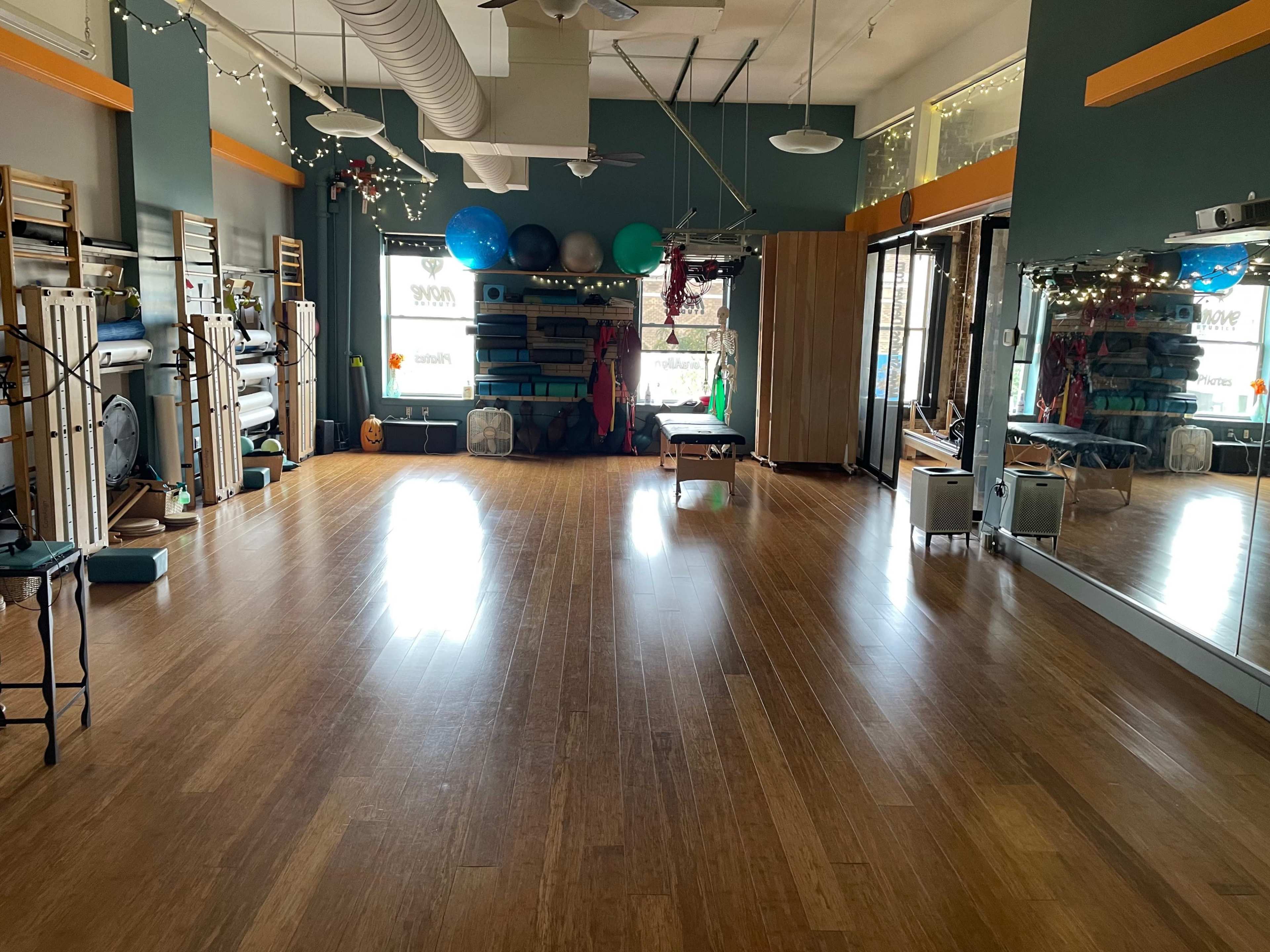 A low-lit studio with wooden flooring, exercise equipment, and large mirrors along one wall.