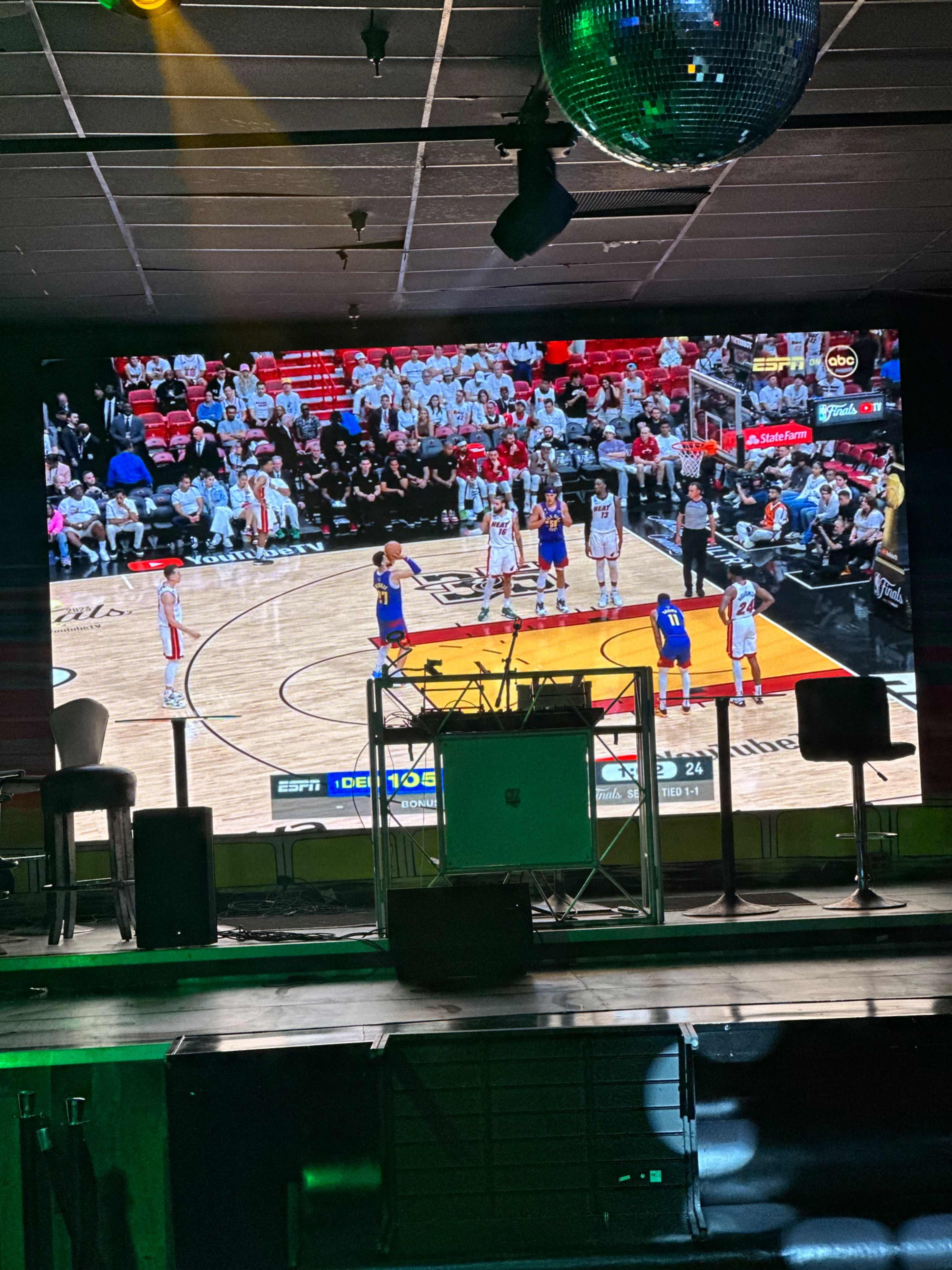A large screen displaying a basketball game with players on the court and spectators in the stands.