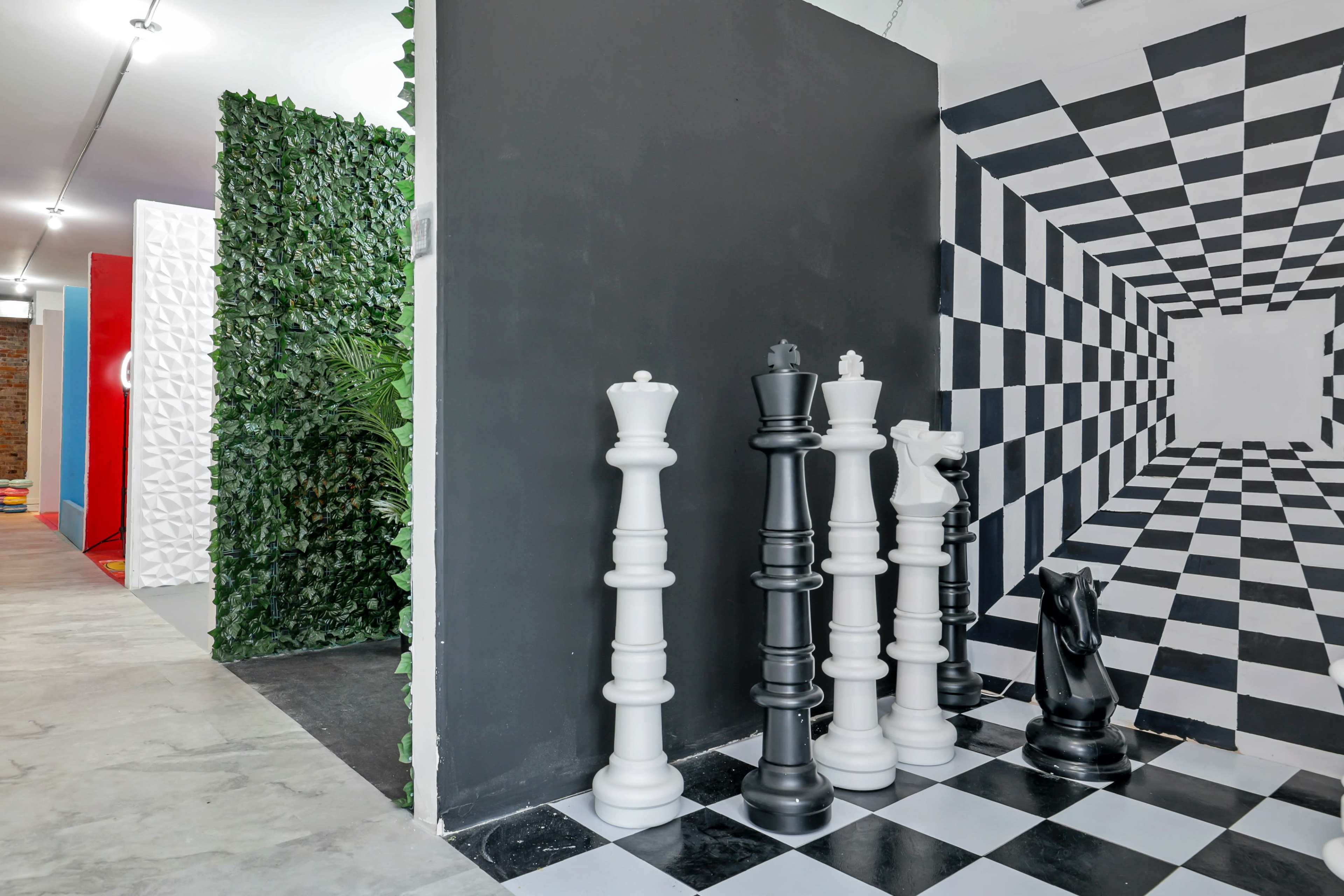 A room with a black and white checkered floor featuring large chess pieces displayed on one side and a mural that creates a three-dimensional optical illusion on the wall opposite.