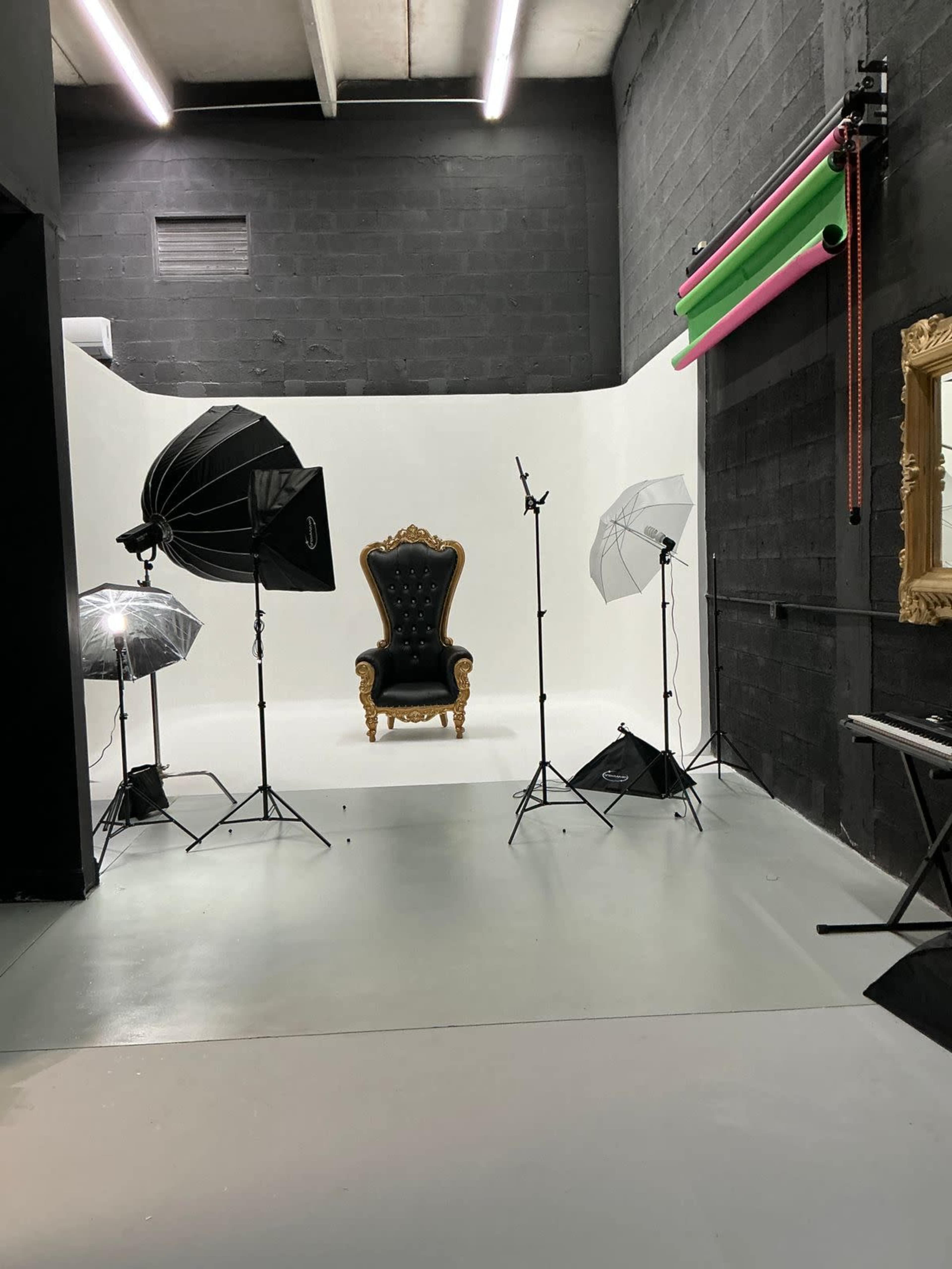 The image shows a photography studio with a central ornate black and gold throne surrounded by various lighting equipment set against a white backdrop.