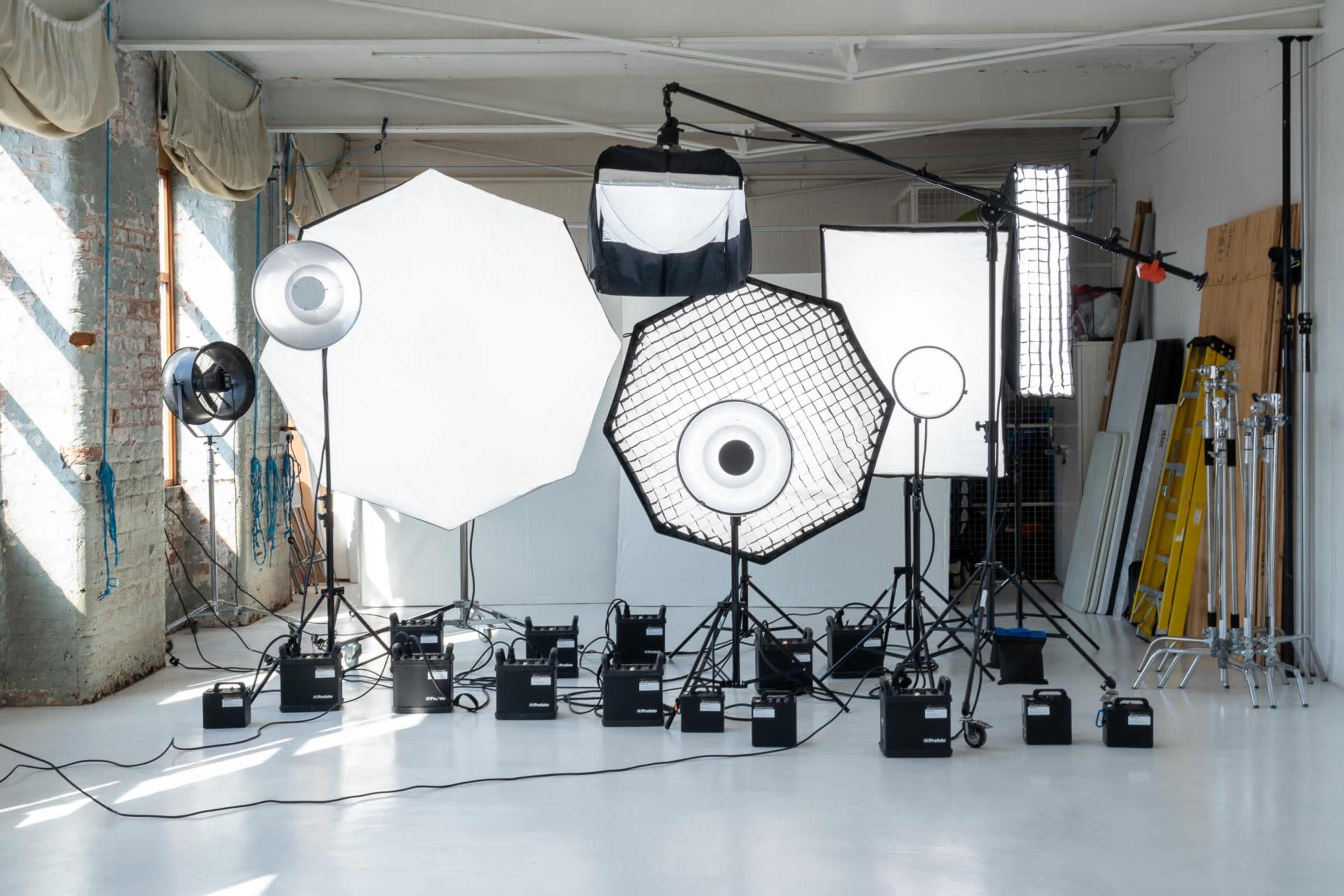 A photography studio is set up with various light sources, softboxes, and light stands arranged on a white floor.